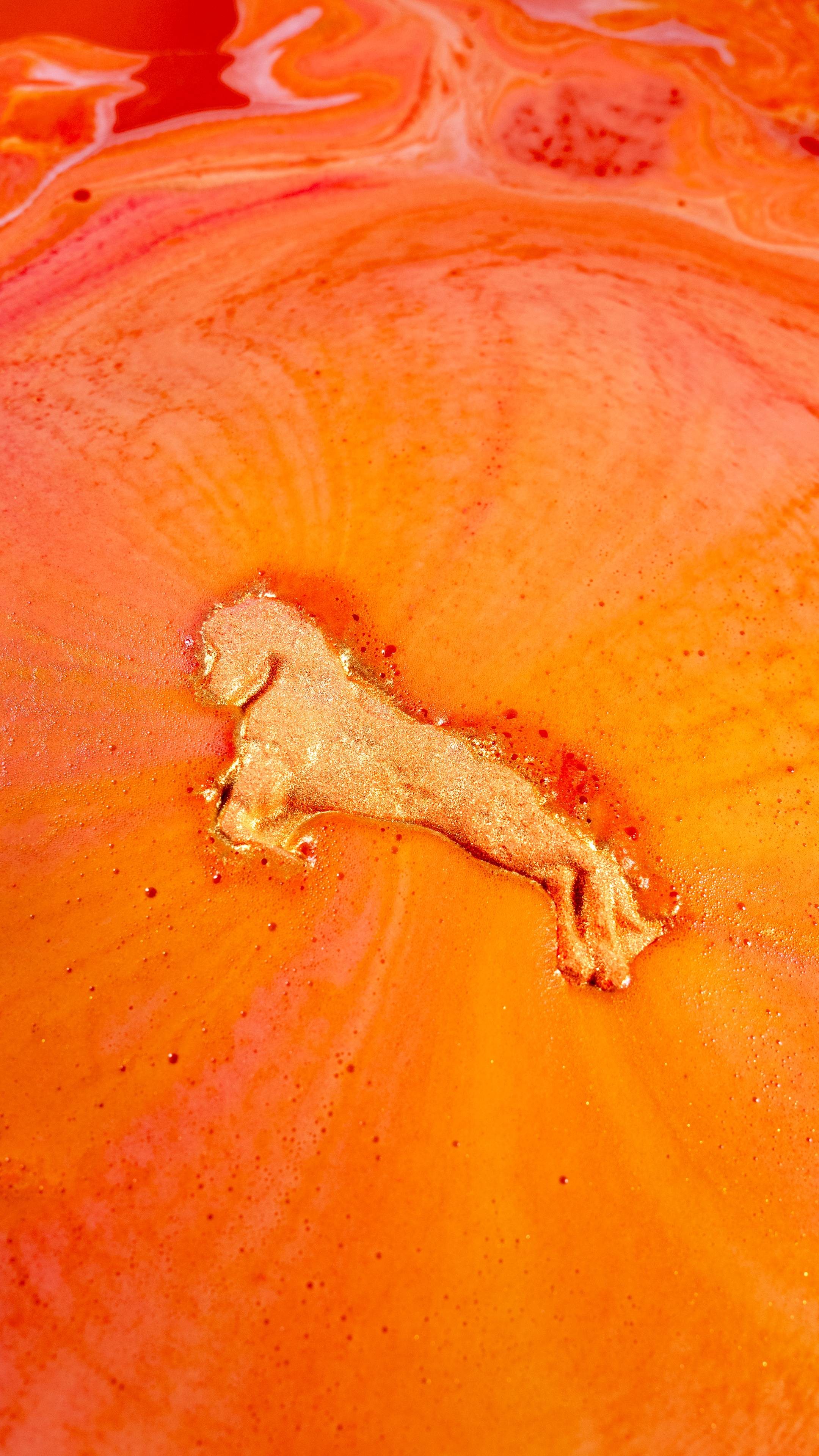 The gold Gallop To Success Bath Bomb dissolves in vibrant orange bath water, releasing swirling foam and shimmering gold Plastic Free Glitter.