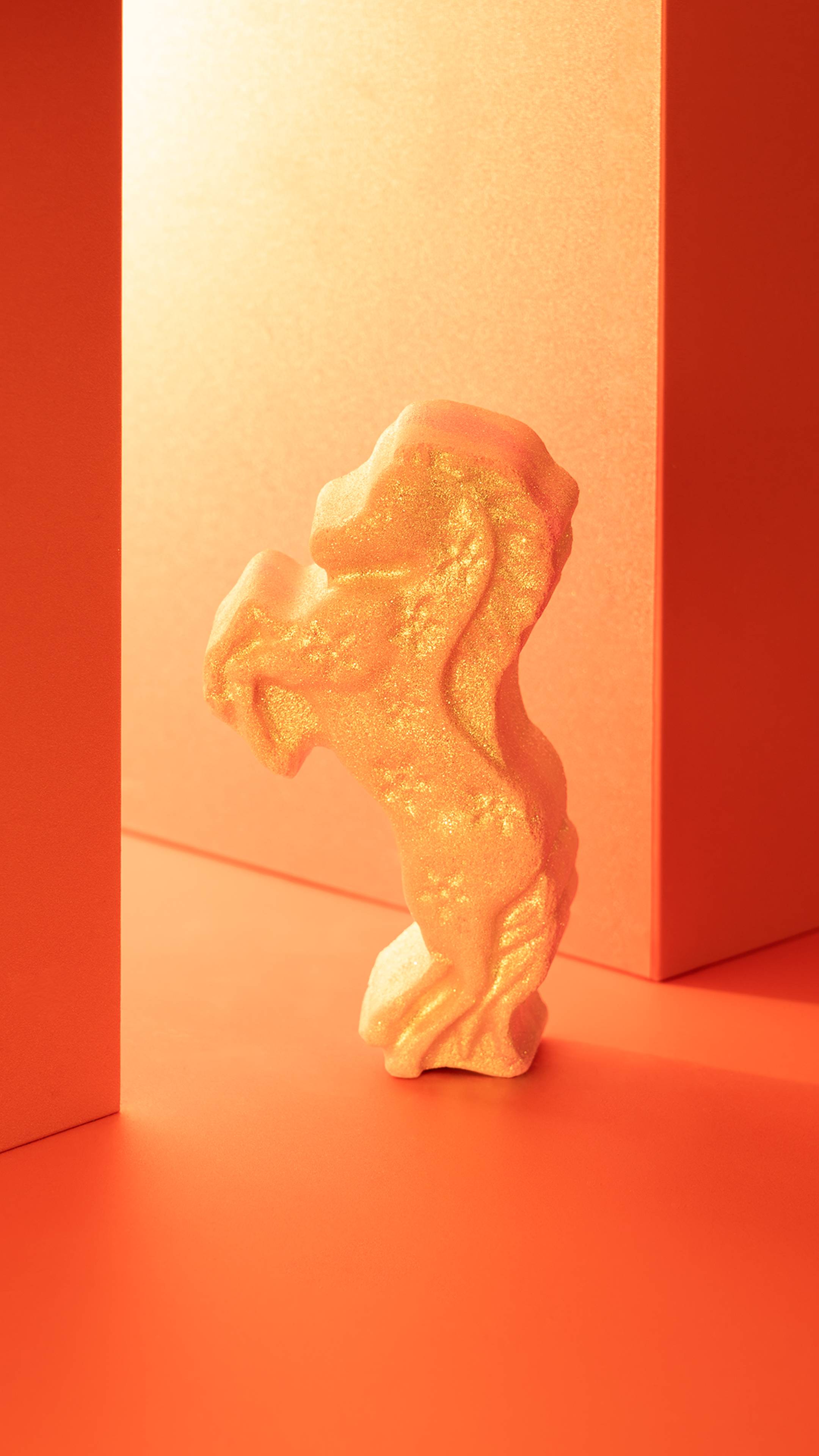 The Gallop To Success Bath Bomb stands upright, showcasing its rearing horse shape and shimmering gold Plastic Free Glitter against a geometric orange background.