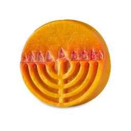 Gelt. A Hanukkah-themed soap. A flat, circular soap slice with a glittering, golden yellow and orange colouring. The shape of a Menorah candelabra is embossed on the front. 