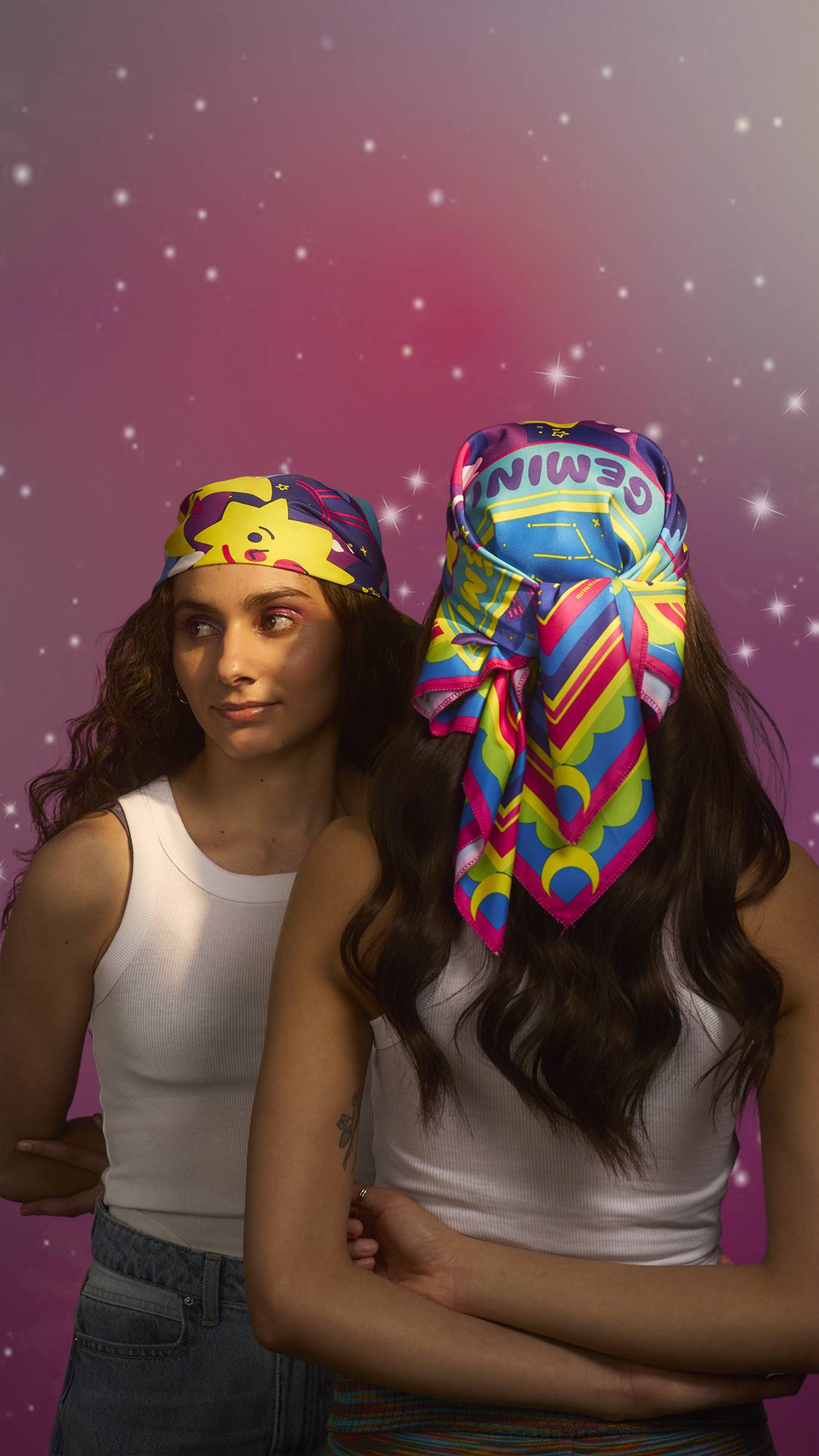 Two similar-looking models wearing the same outfit with the same hairstyle have fashioned the Gemini knot wrap into a stylish head bandana and are standing facing towards and away from the camera to show each angle. 