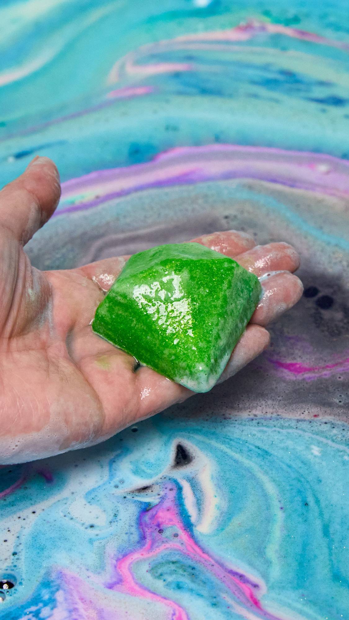 The Giant Intergalactic bath bomb has fully dissolved leaving behind colourful swirls of foamy water as the model holds a surprise, green diamond-shaped soap gift in the centre. 