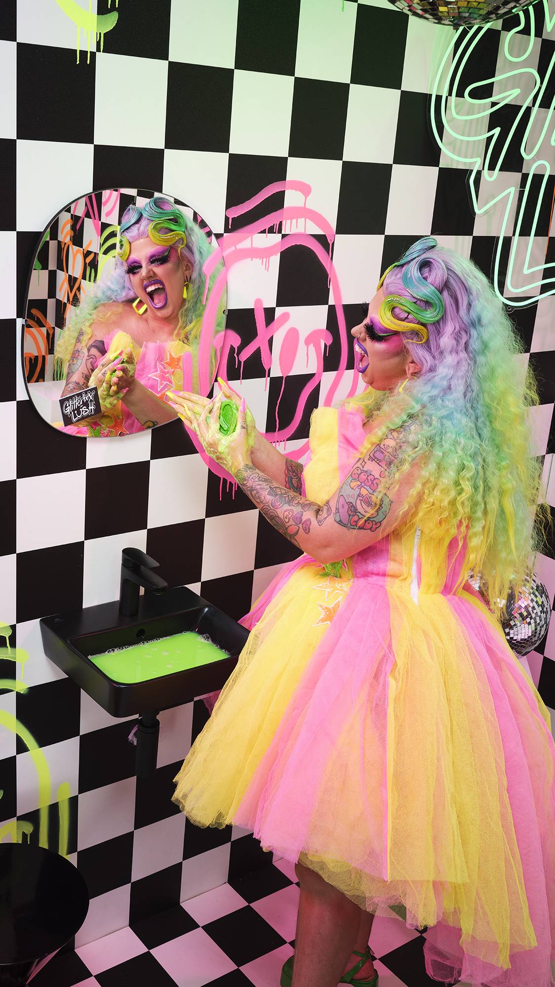 Model is stood in a checkered room with neon graffiti. They wear bold colours as they wash their hands with the green soap.