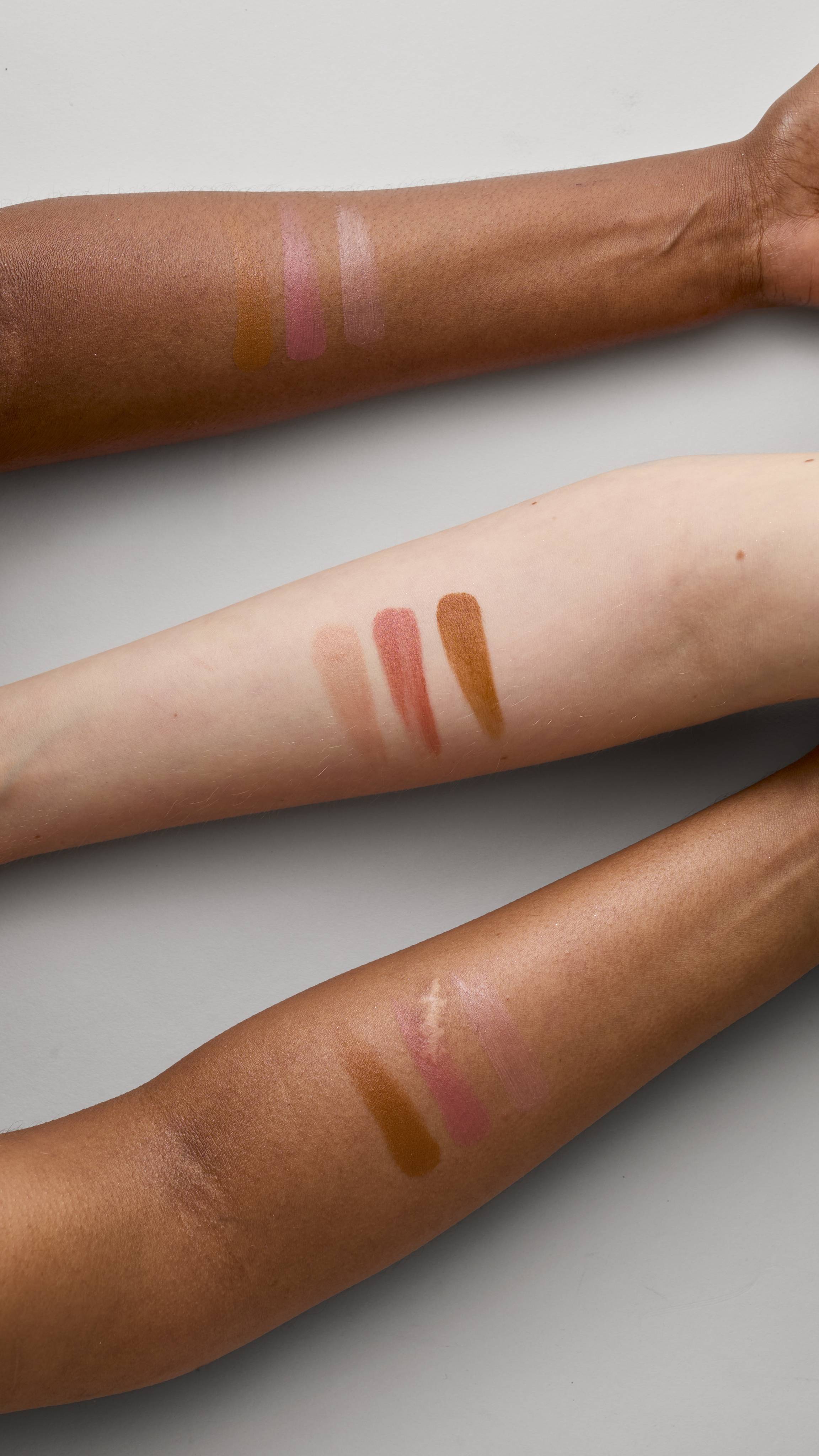 Three forearms with various complexions are shown on a light grey background. Each has three swatches of Glam Nudes ~ Lip square product, including shades of terracotta brown, peachy nude, and shimmering champagne nude.