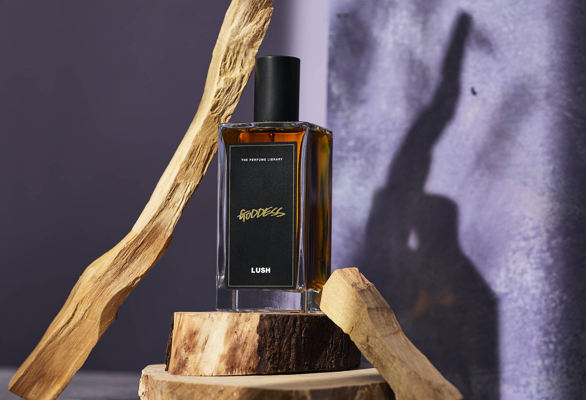 A dark amber coloured bottled perfume, Goddess, sits on top of a display of sandalwood, one of it's main ingredients.