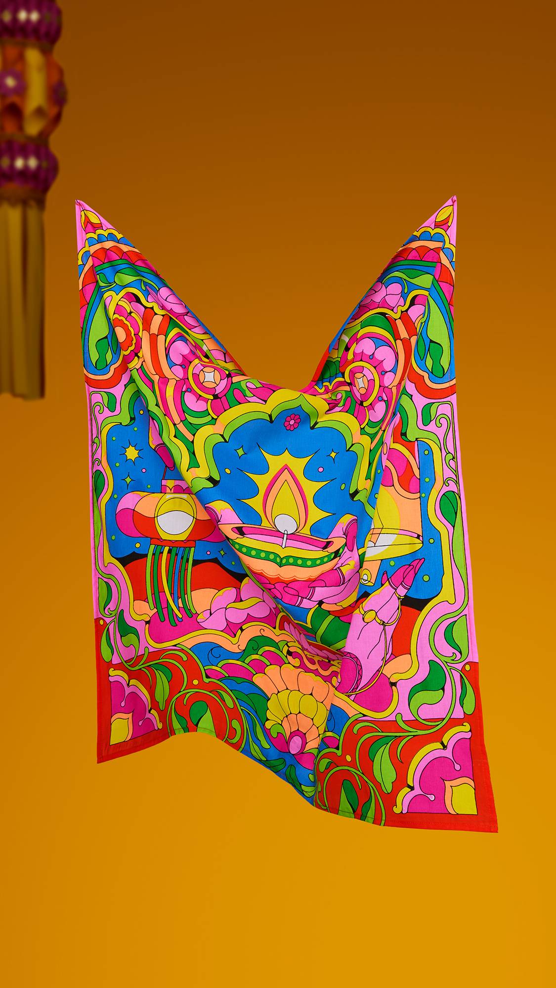 A vibrant, colourful Lush "Golden Glow" Knot Wrap floats against a warm orange background, displaying a psychedelic stained-glass design of a glowing diya flame, paper lanterns, and intricate pink, green, and blue patterns.