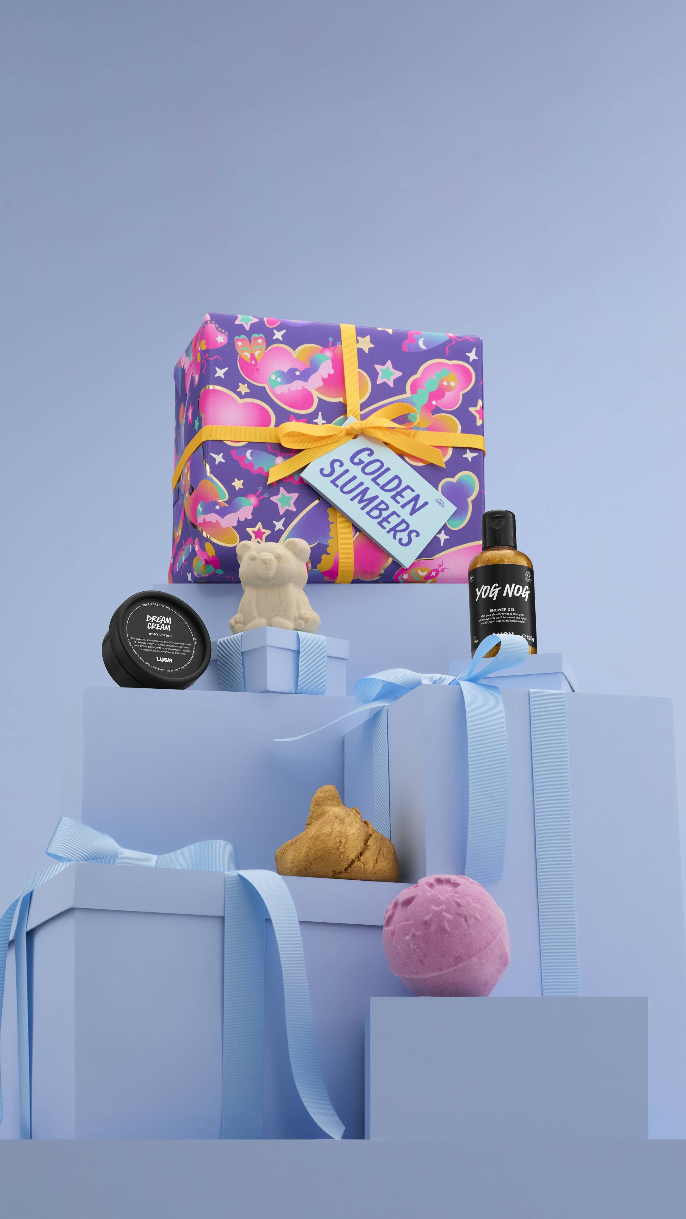 The image shows a large pile of differently-sized wrapped pale-blue gifts with ribbons, on a matching blue background. The purple "Golden Slumber" gift box sits on top, and the five products sit on lower blue gifts. 
