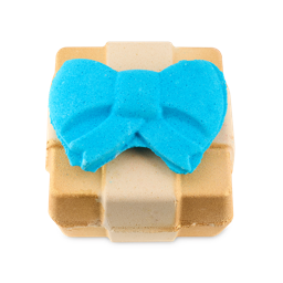 Golden Wonder 3-in-1 bath bomb. A cuboid bath bomb shaped like a golden gift box wrapped in ribbon. A bright blue, removable bow sits prominently on top.