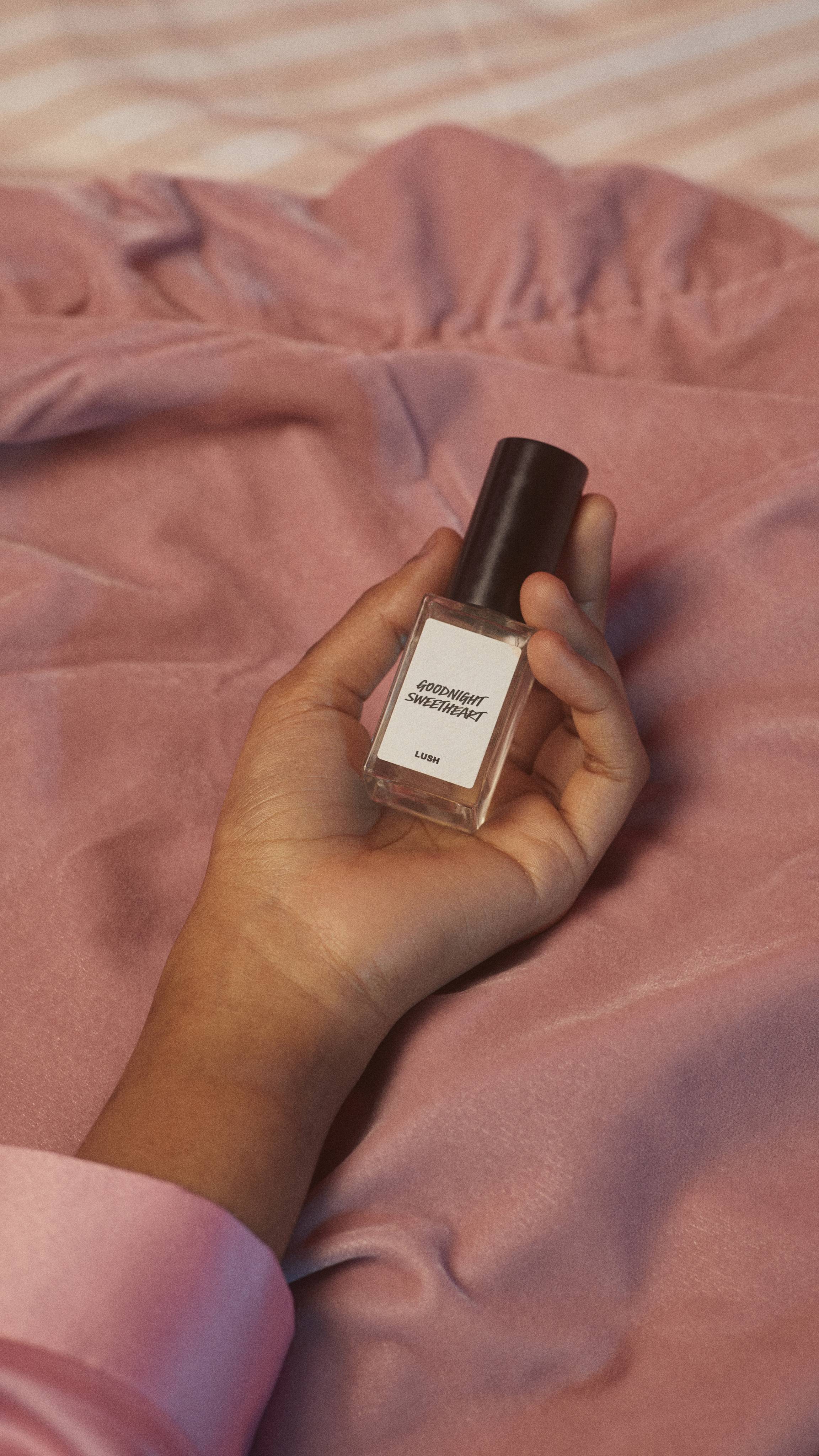 A close-up image of the model's hand gently holding the Goodnight Sweetheart glass bottle on a dusky pink blanket.