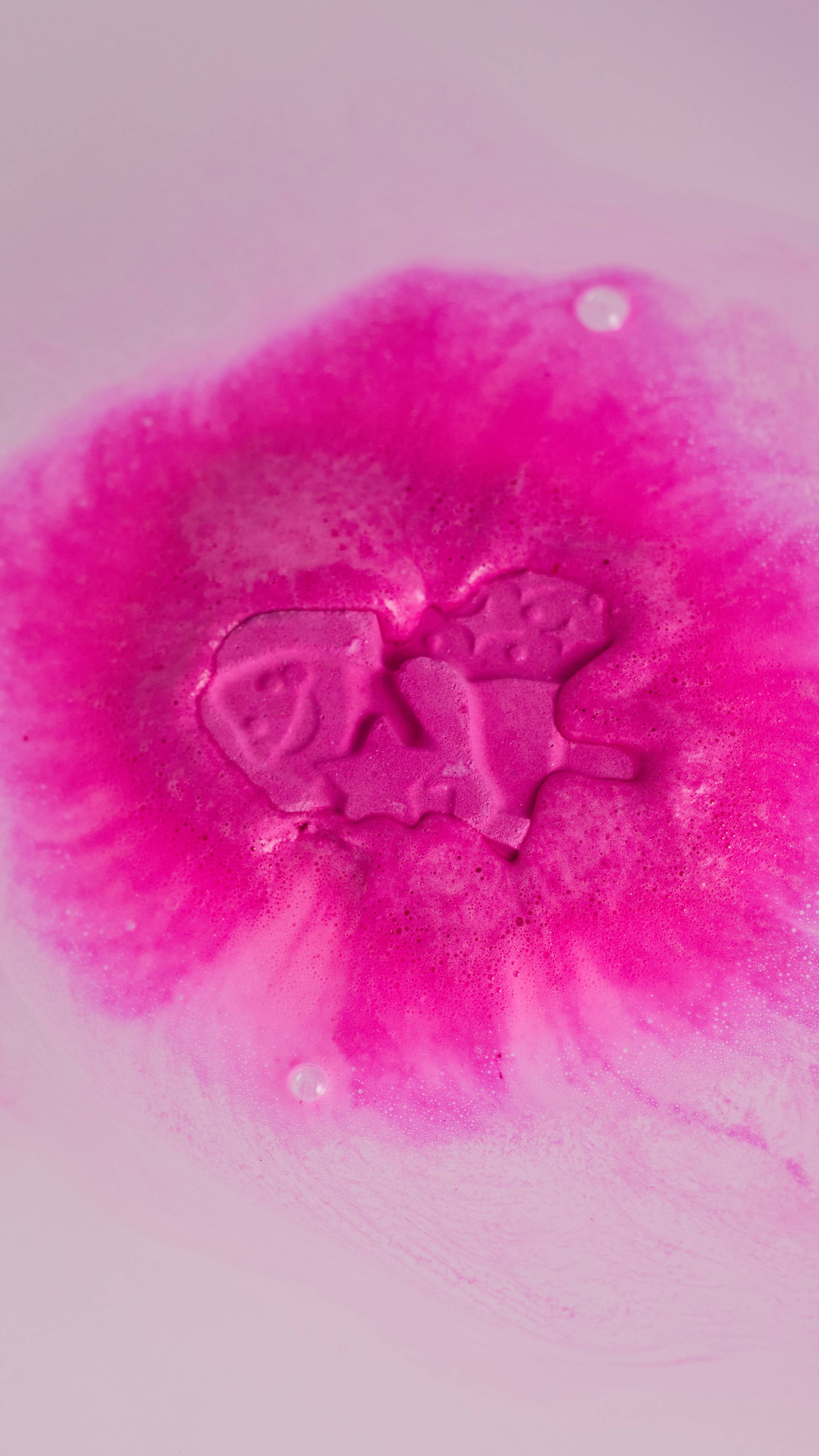 The Groovy Fairy bath bomb has just been placed in the bath. The vivid fuchsia is melting out into the clear water.