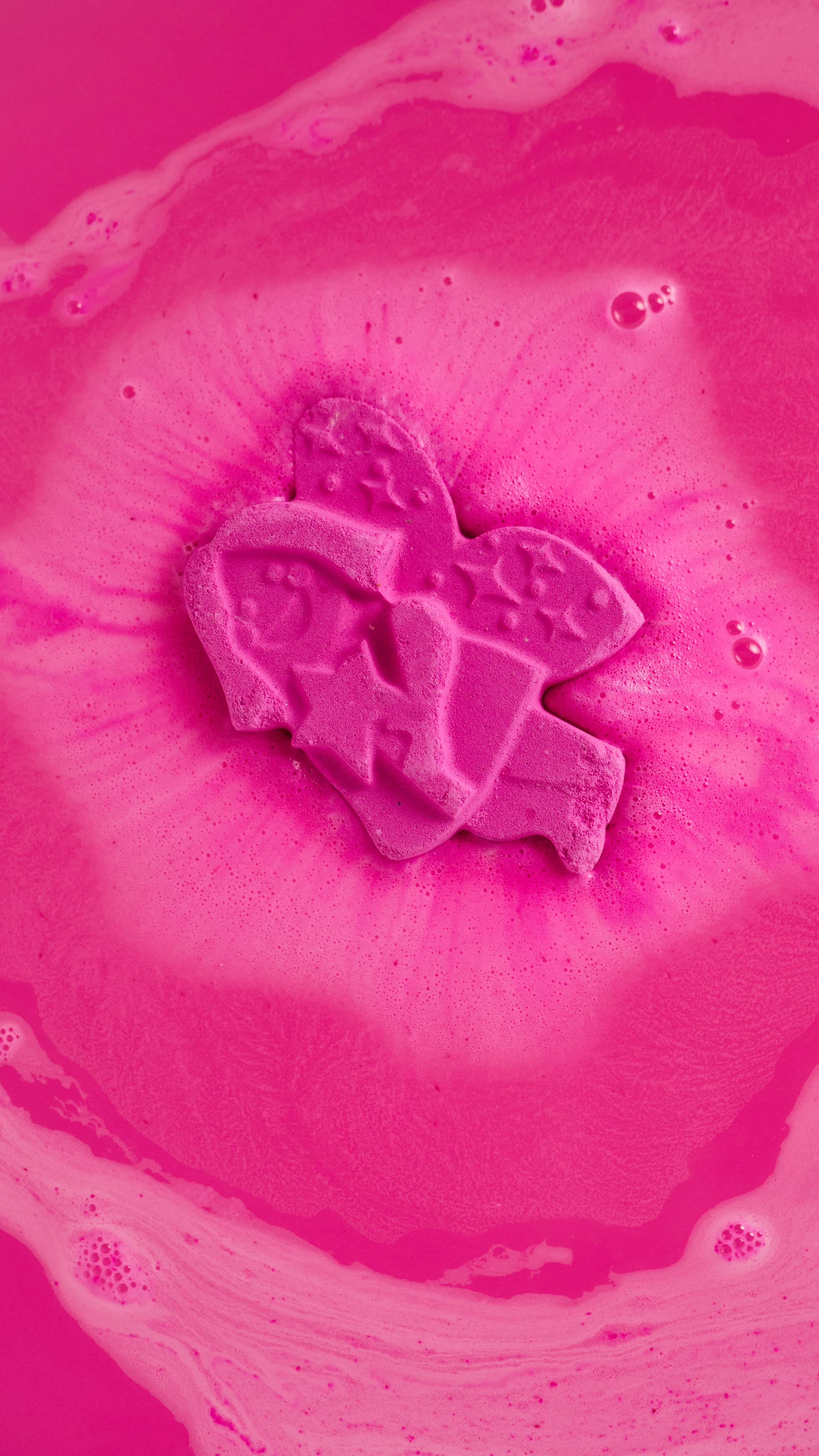 Groovy Fairy bath bomb is melting into the bath water creating layers of deep pink, foamy swirls.