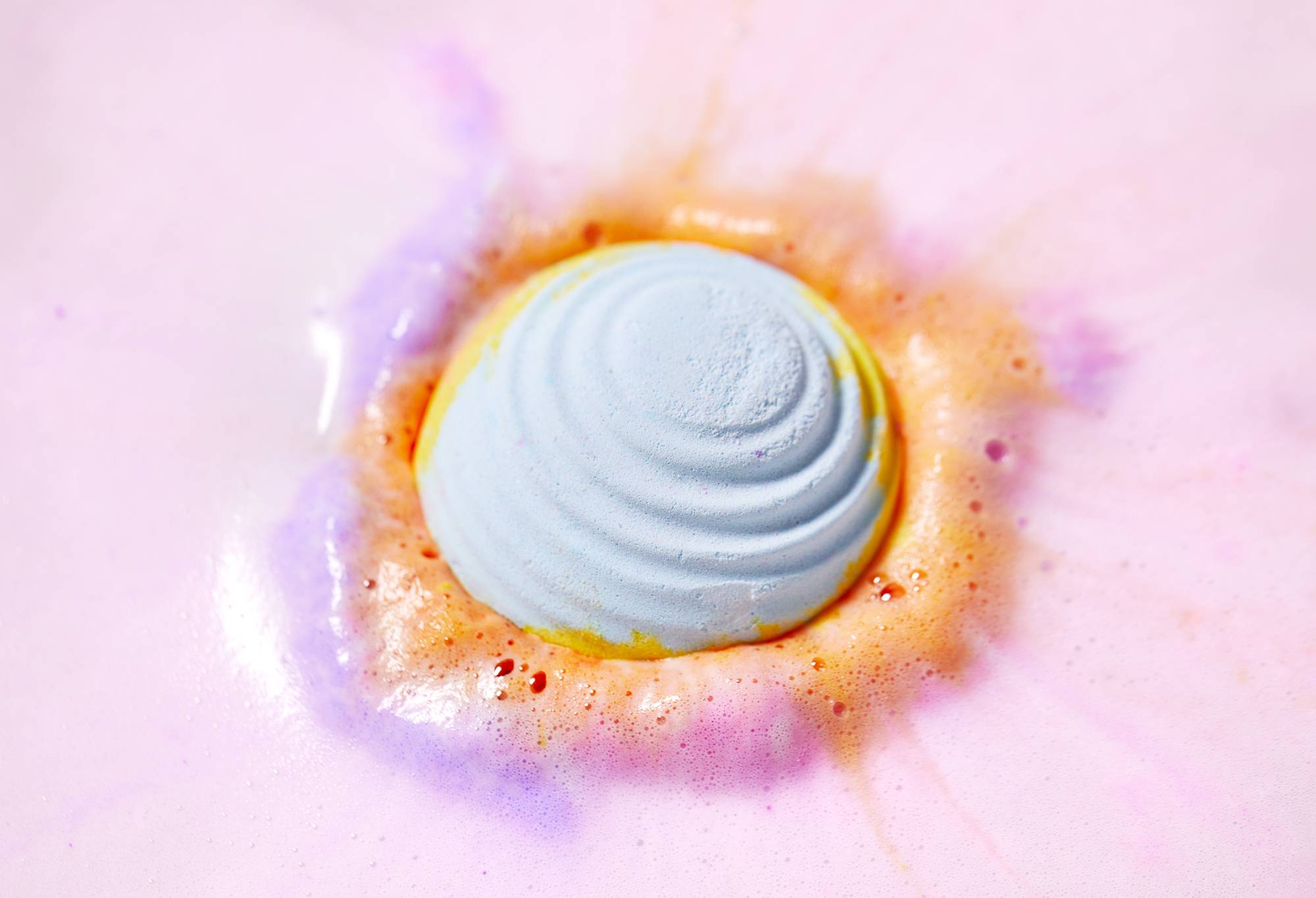 Unicorn Poop bath bomb floats among a velvety blanket of soft pink and orange foam bubbles.