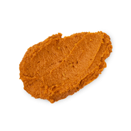 A textured, oval-shaped swatch of thick Lush Halloween Queen face mask against a white background. The bright orange paste has a rough texture, filled with numerous tiny exfoliating specks and small organic fragments.