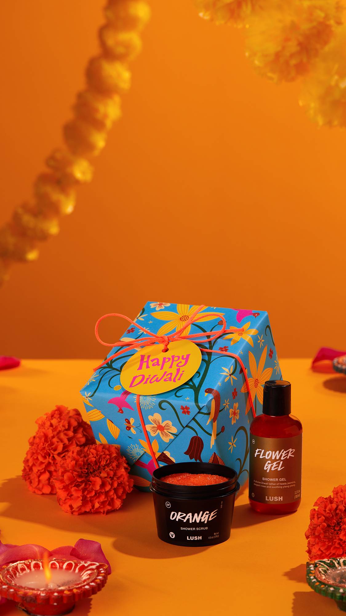 The Happy Diwali gift-wrapped box sits with the shower gel and body scrub on a bright orange background draped in marigolds.