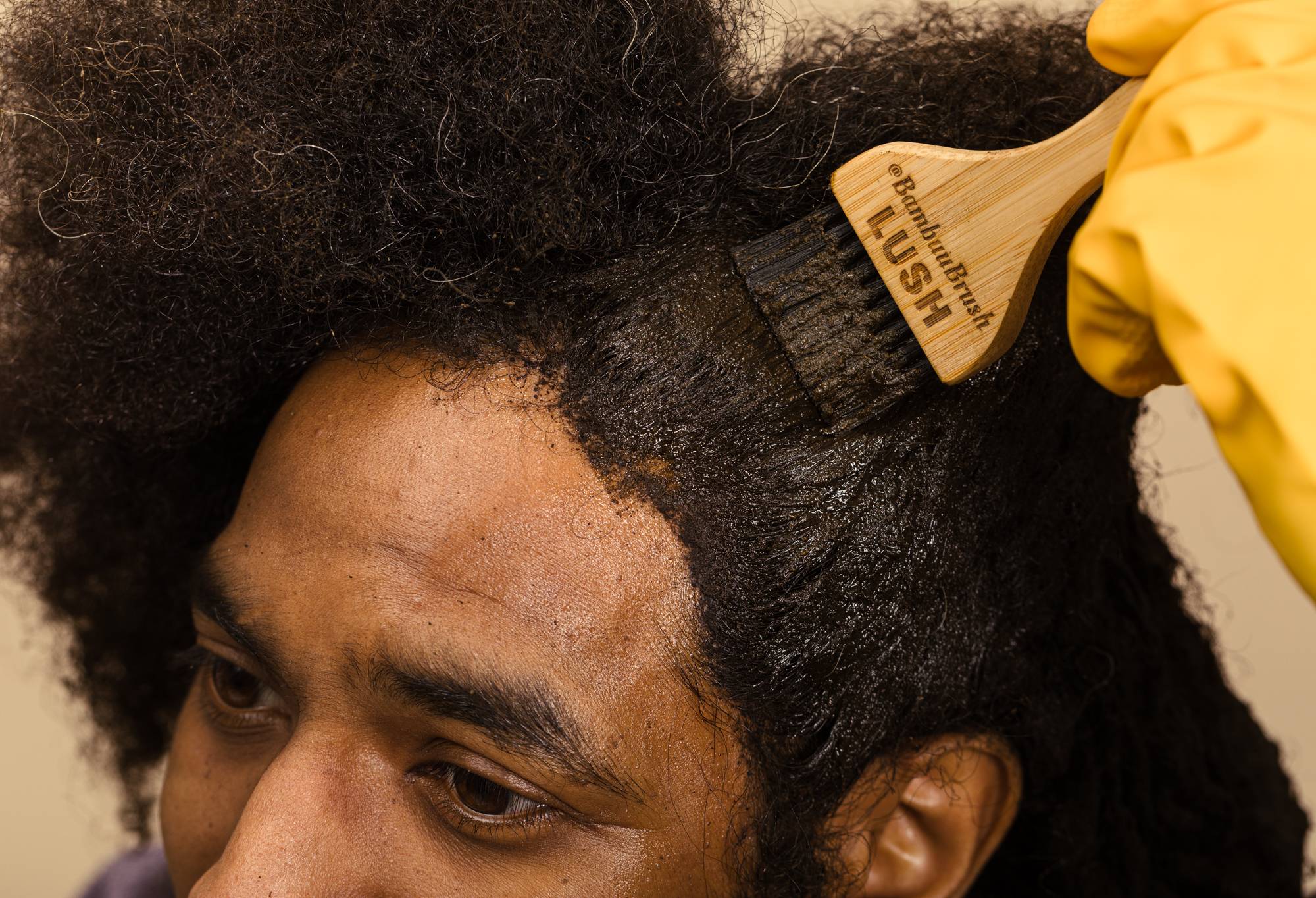 The brush is used to evenly apply fresh henna to the hairline of a model's dark afro hair.