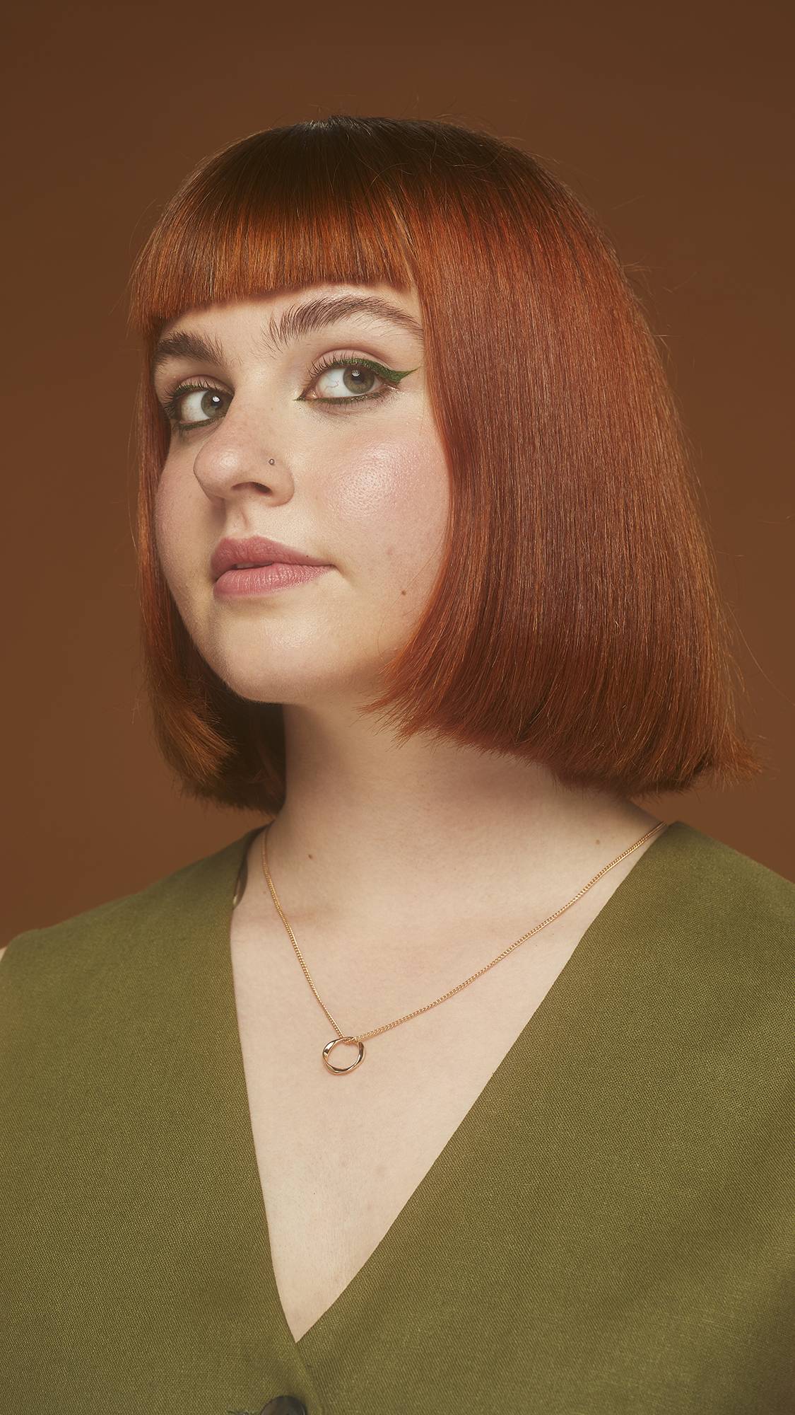Image shows model on an earthy background. They have bold eyeliner with their hair showing deep reds, browns and coppers.