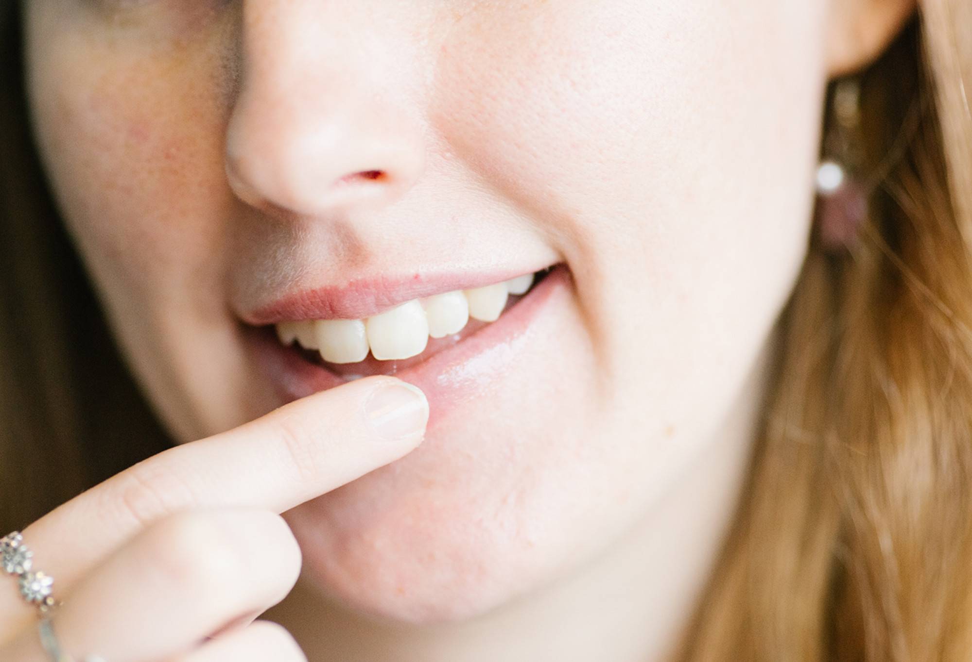 A finger glides Lip Service lip balm onto soft, shiny, smiling lips.