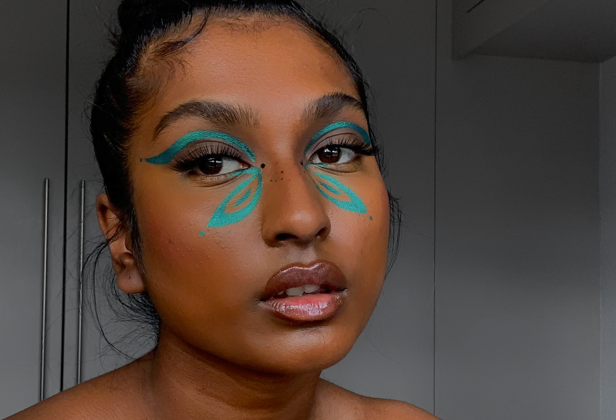 A person with a stunning, butterfly-like design painted onto their face, using shimmery aquamarine blue Motivation eyeliner.