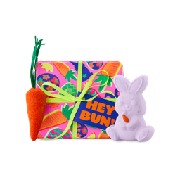Hey Bun! A pink wrapped box with carrot patterns, a lime green ribbon, and a "HEY BUN!" tag. Two included gift products, a bunny-shaped bath bomb and a carrot-shaped bubble bar, sit around the box. 