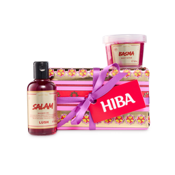 Hiba. A selection of Lush Eid products, including a bottle of "Salam" shower gel, a pot of "Basma" body scrub, and the "Hiba" gift set. The gift is wrapped in gold and pink patterned paper with a purple ribbon and a red "Hiba" gift tag.