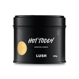 Hot Toddy. A front shot of a short, cylindrical-shaped black tin with a matching lid. There is a black label across the front with the Words "Hot Toddy" and a gold, circular, Lush Community sticker to the side. 