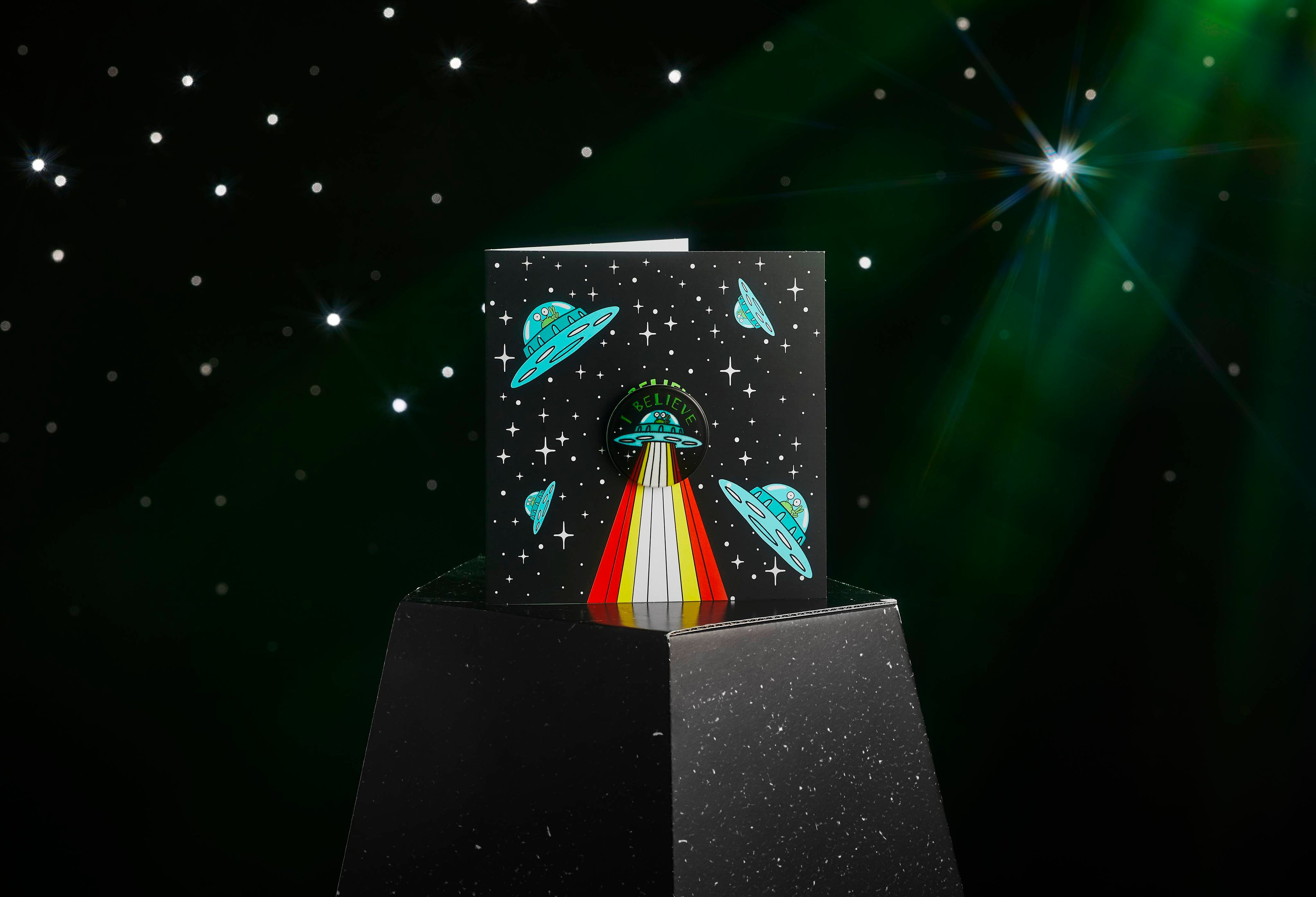 Image shows the I Believe greetings card displayed on a stand on an emerald, twinkling background. 