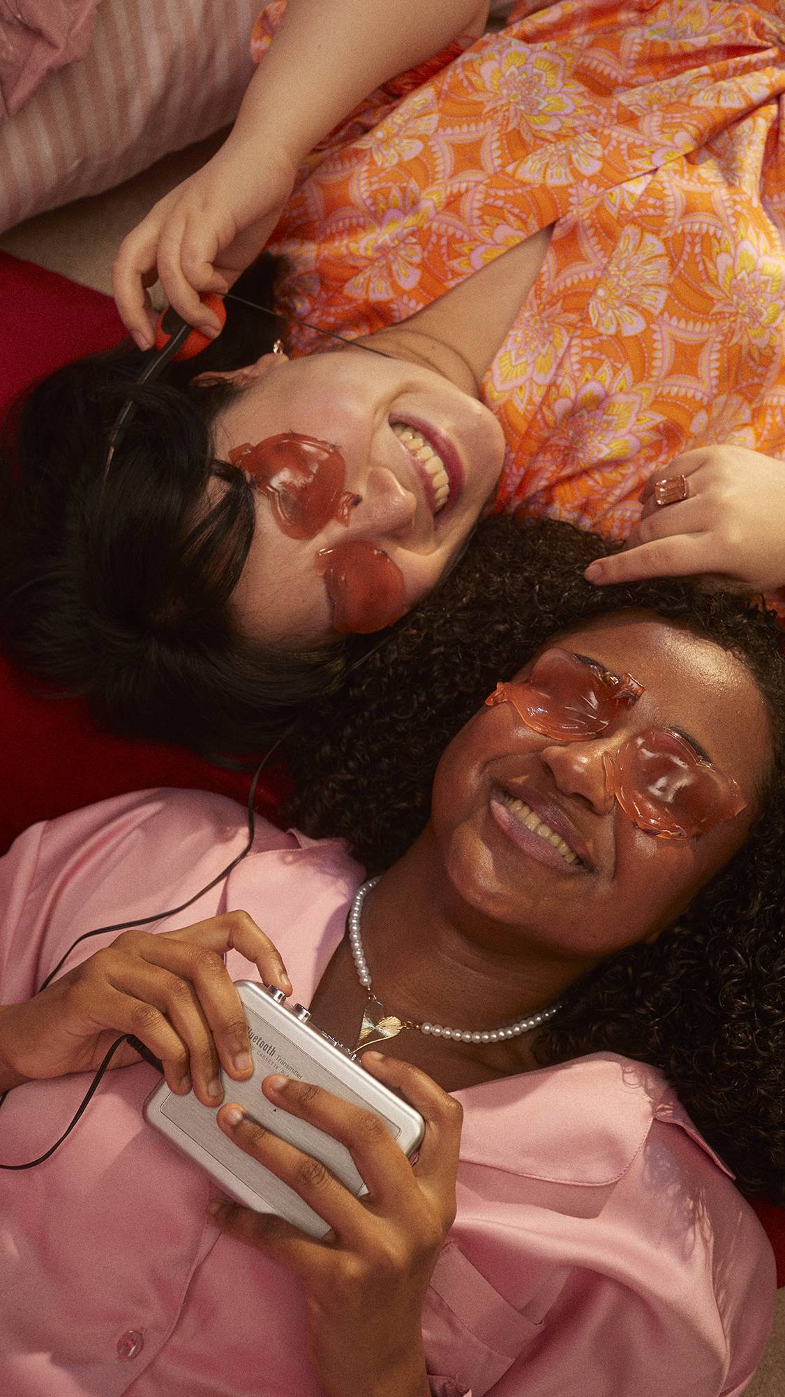Two models lay down with their heads together, smiling, as they both wear the I Heart You eye pads.