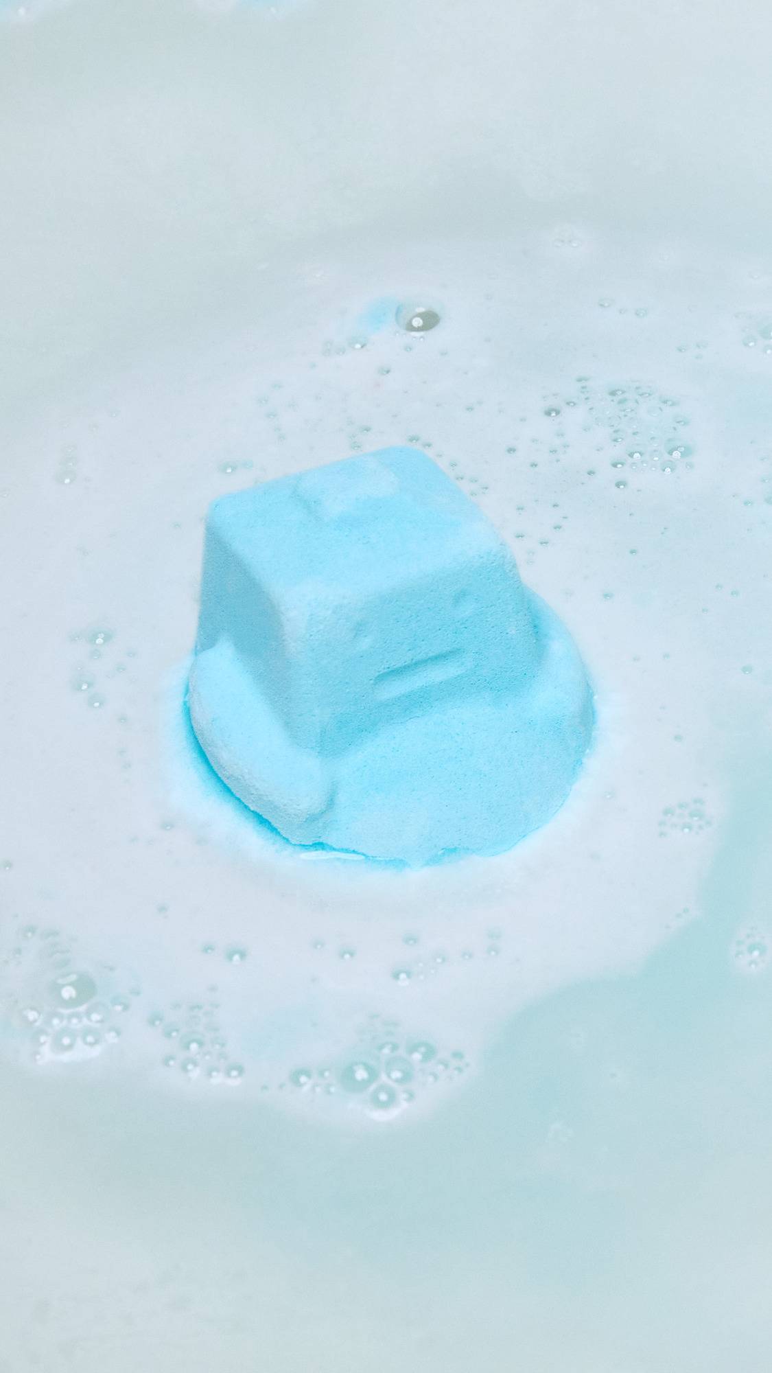 The Ickle Baby Bot bath bomb has been gently placed into the bath water and is beginning to give off blue water and thick, crisp foam. 