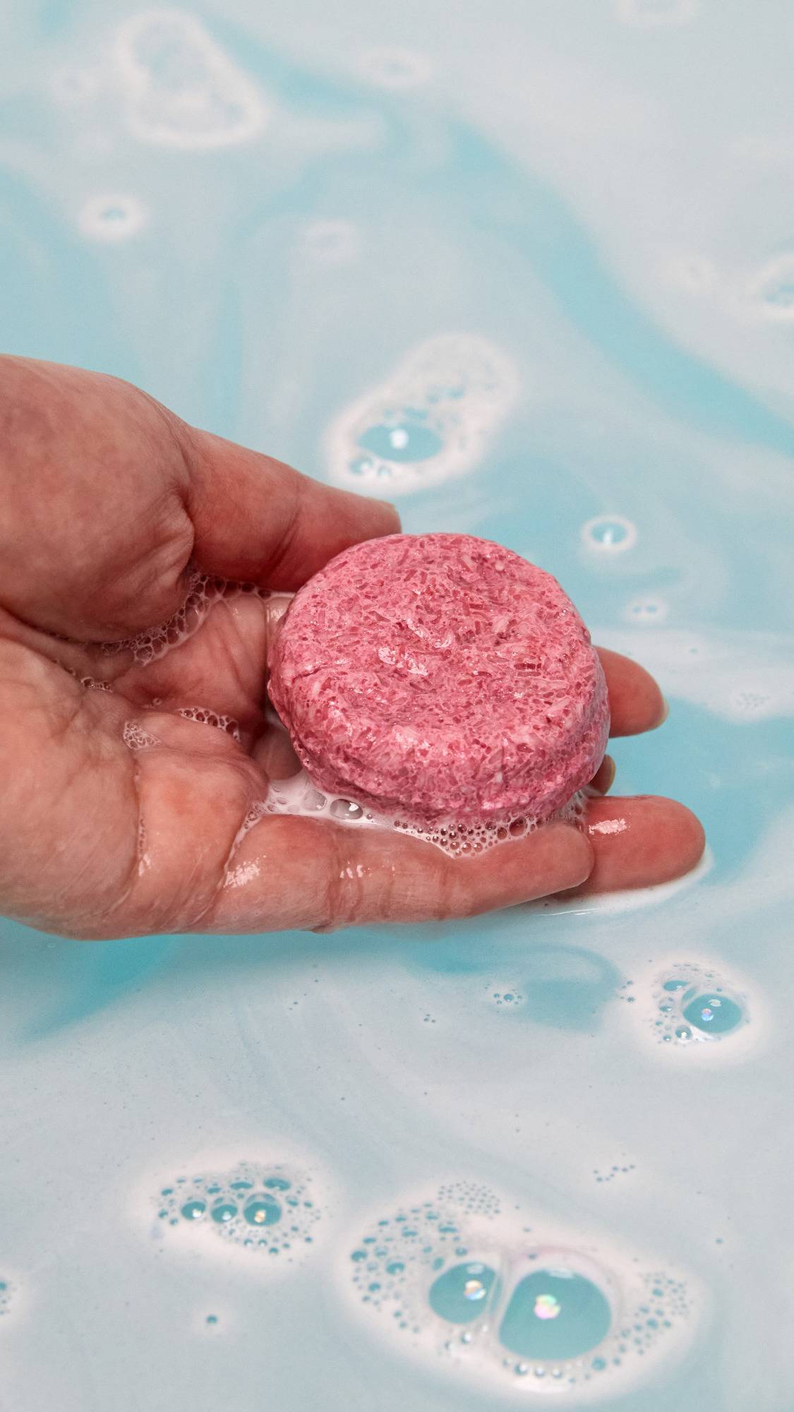The Ickle Baby Bot bath bomb has completely dissolved in the water leaving behind a surprise mini reusable shampoo bar help by the model above sky blue waters. 