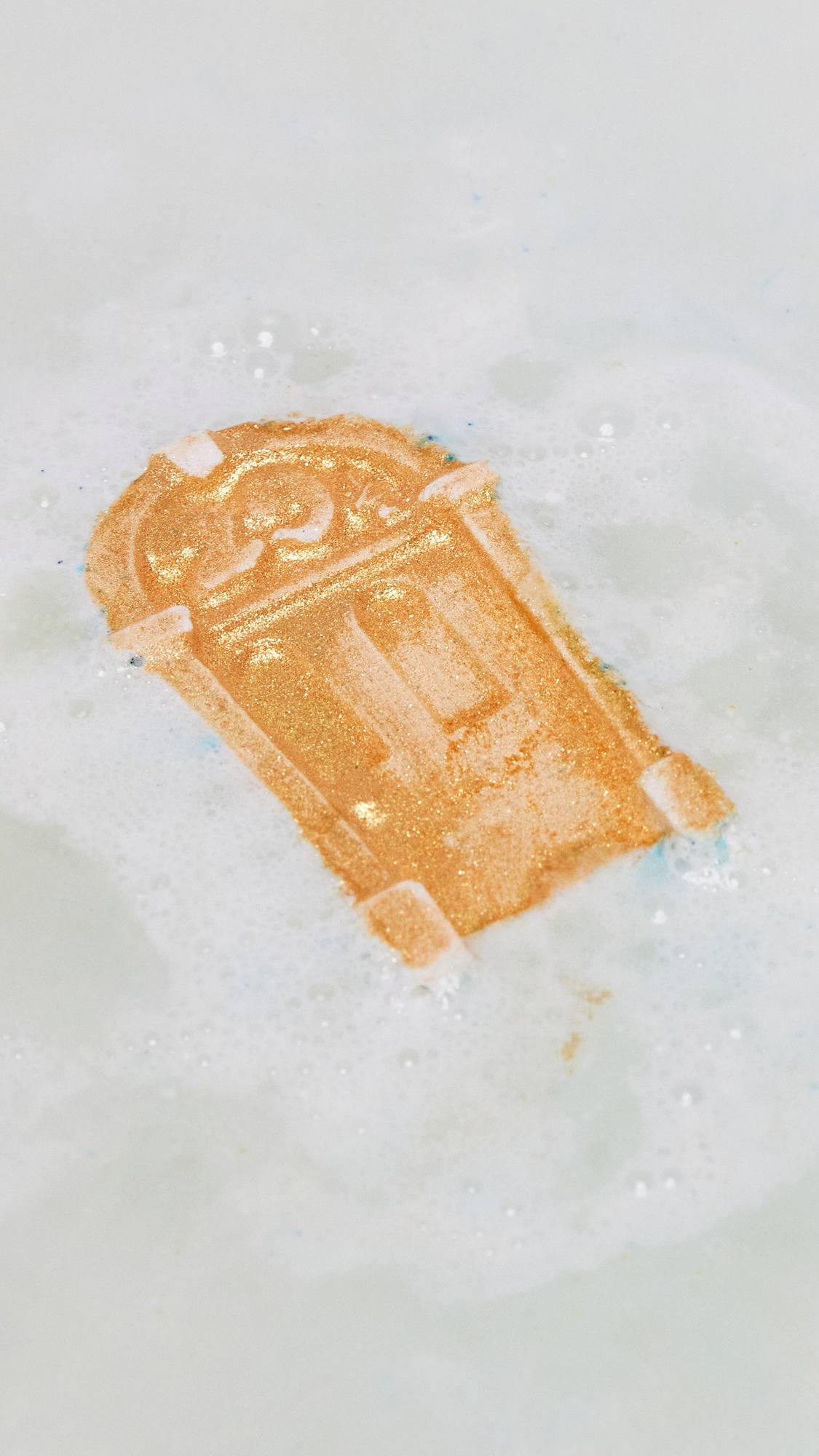 The Iconic Door bath bomb has been gently placed into the bath as it creates delicate teal waters and light foam as the golden lustre sits on top of the water. 