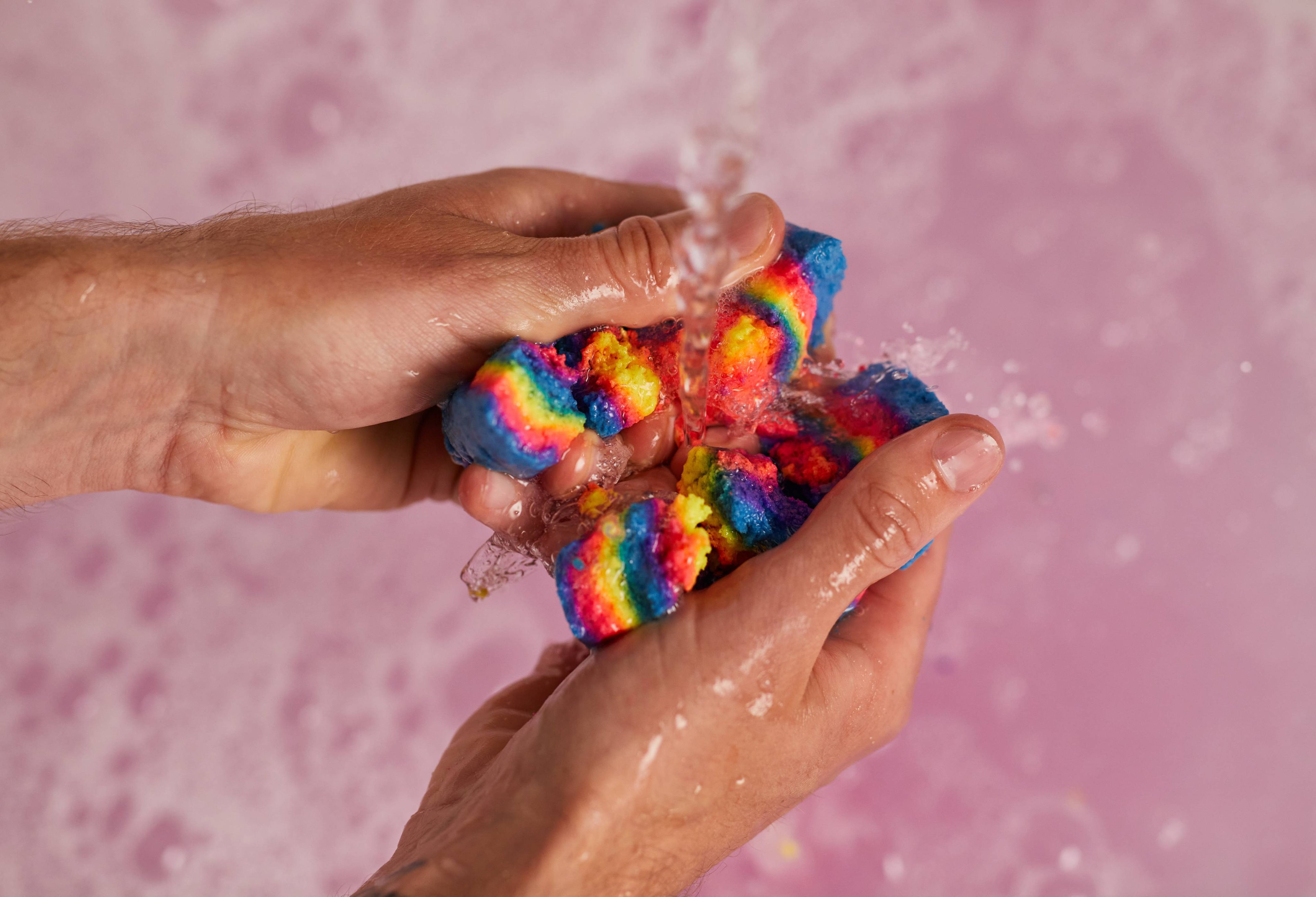 Image shows the model crumbling the Intergalactic bubble bar with both hands under running water. 