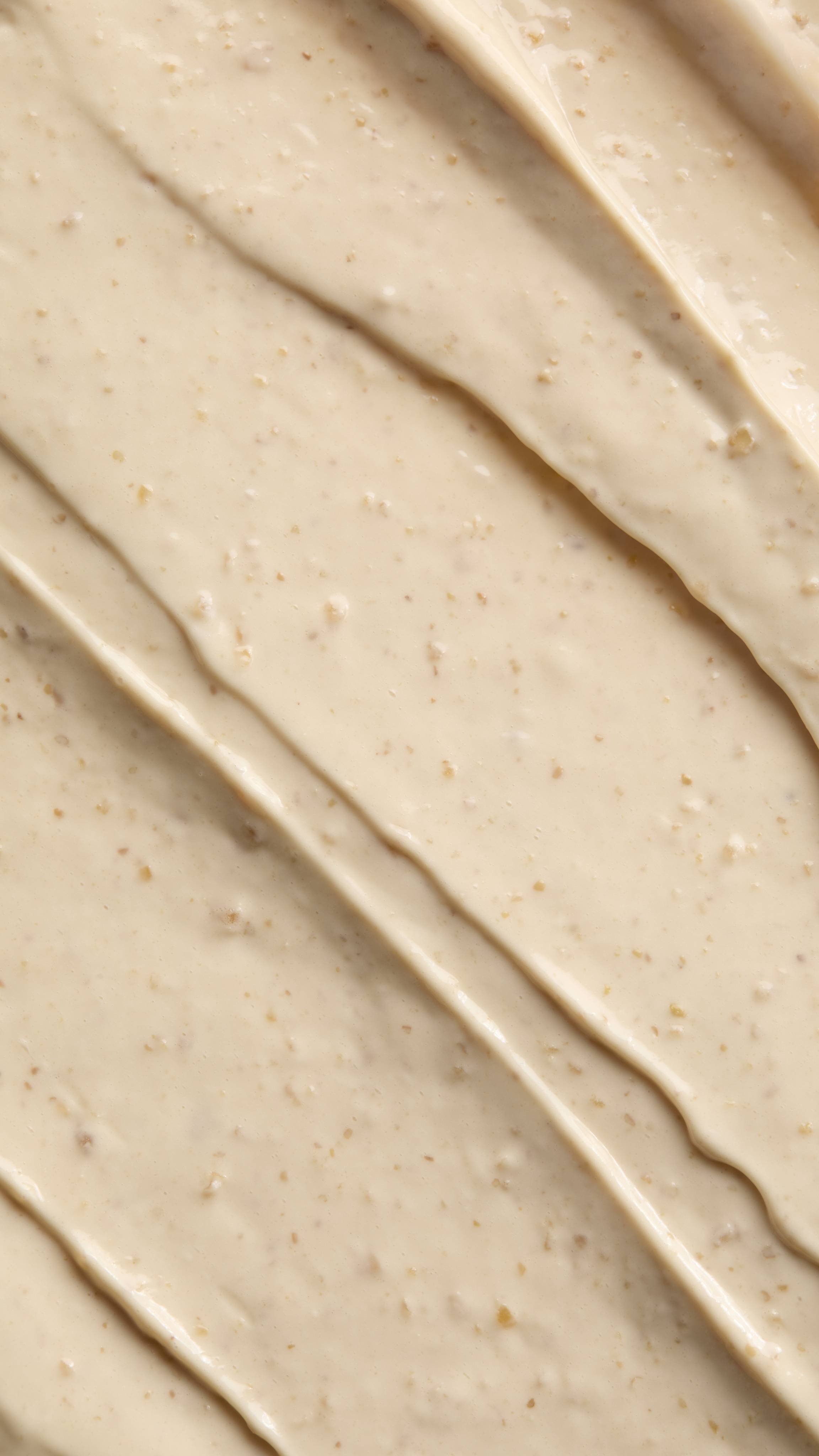 Extreme close-up of a smooth, creamy light-beige Jack O Lantern Fresh Hair Food product spread out with soft diagonal ridges, showing fine exfoliating specks throughout the texture.