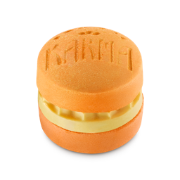 Karma. An orange, circular bath bomb shaped like a macaron with a creamy yellow middle layer of solid oil. The word 'KARMA' is embossed on the top surface, which is dusted with a fine gold shimmer.
