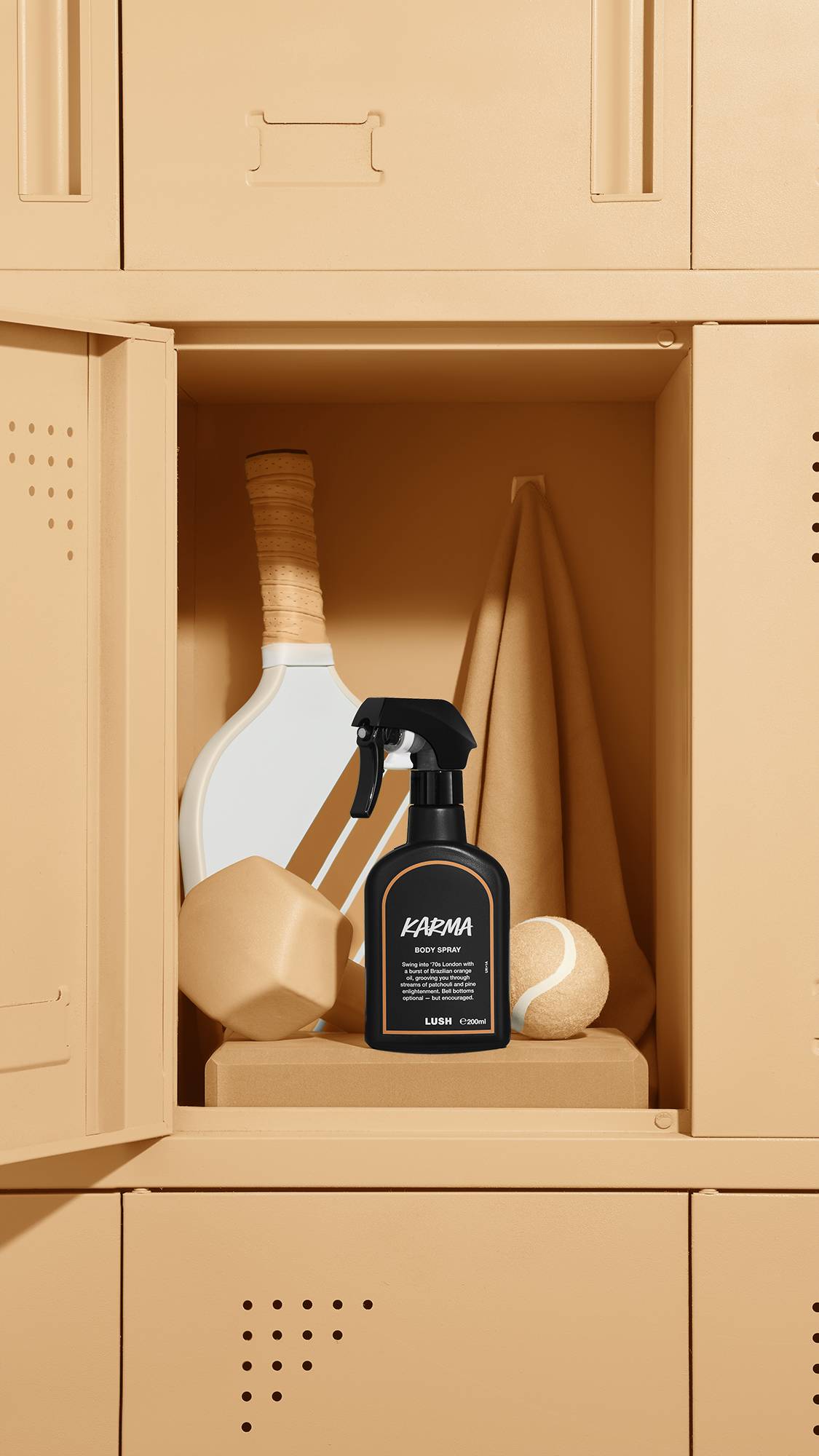 The image shows a black LUSH 'Karma' body spray bottle with an orange rimmed label, standing inside an open beige locker. A tennis racket, a beige towel, a weight, and a tennis ball are also visible within the locker.