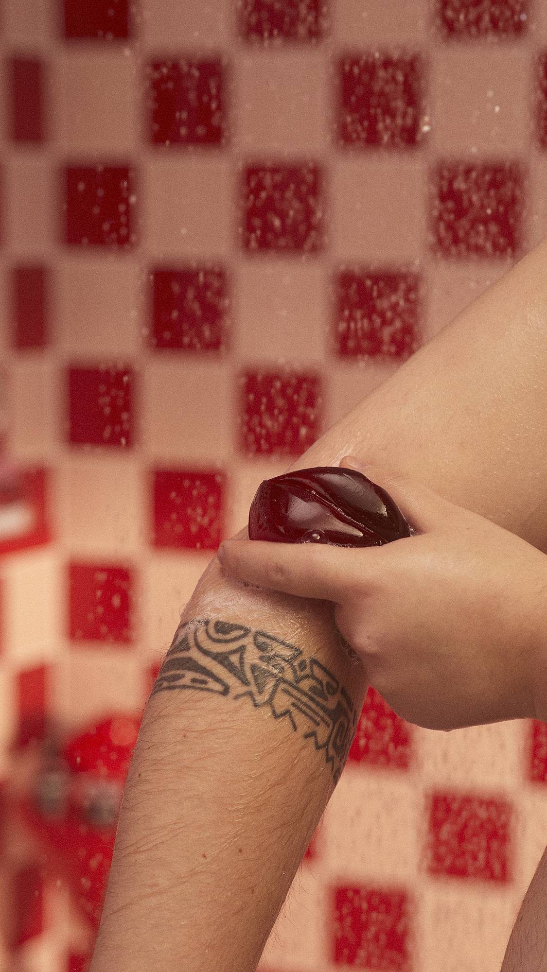 A close-up image of the model's arm under running shower water as they lather up their forearm with the Kiss Me Quick shower jelly.