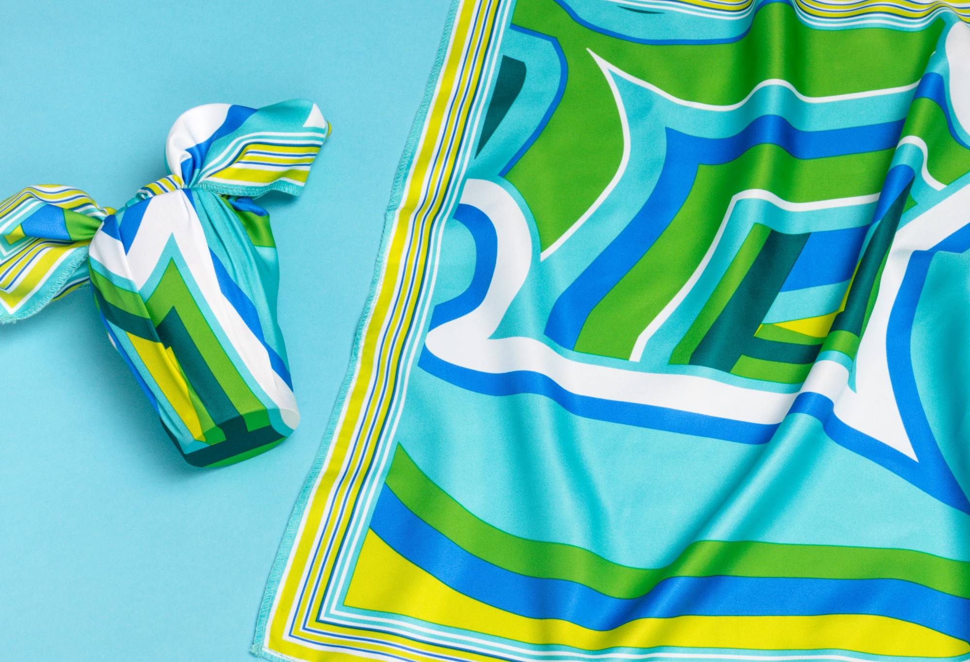 The knot wrap is wrapped and knotted around a perfume bottle, as well as laid out flat, on a light blue background.