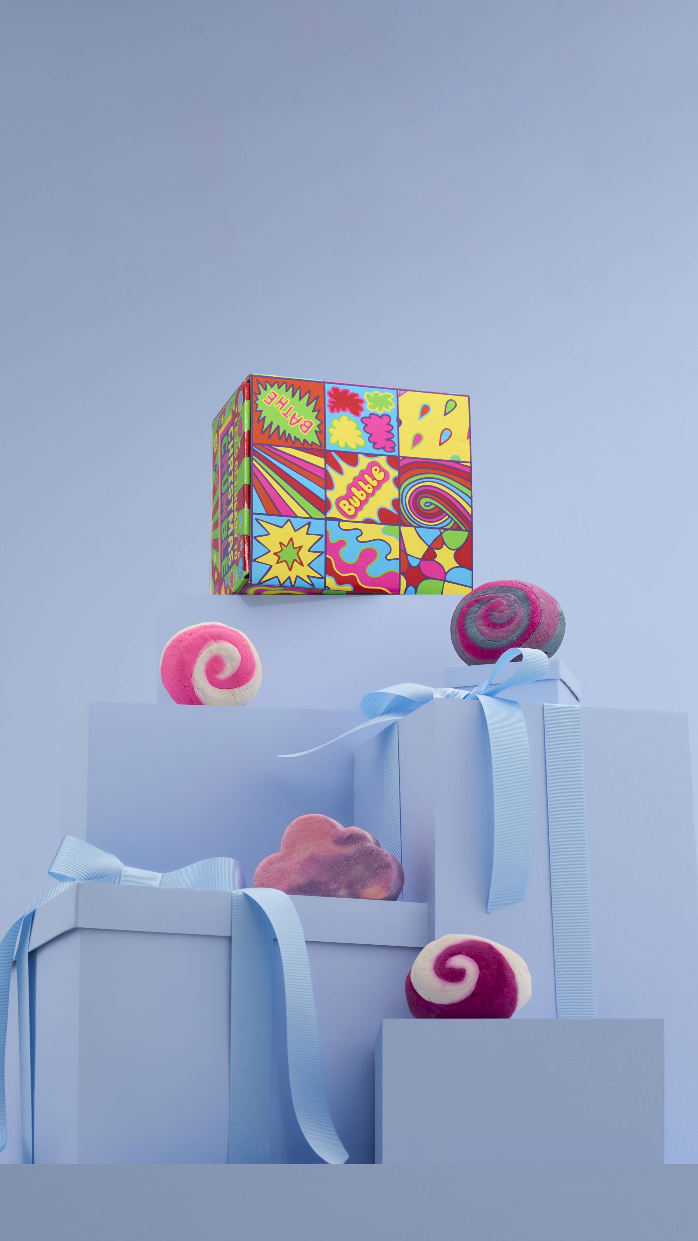 The image shows a large pile of differently-sized wrapped pale-blue gifts with ribbons, on a matching blue background. The colourful "Let's Get Ready to Christmas Crumble" gift box sits on top, and the four products sit on lower blue gifts. 