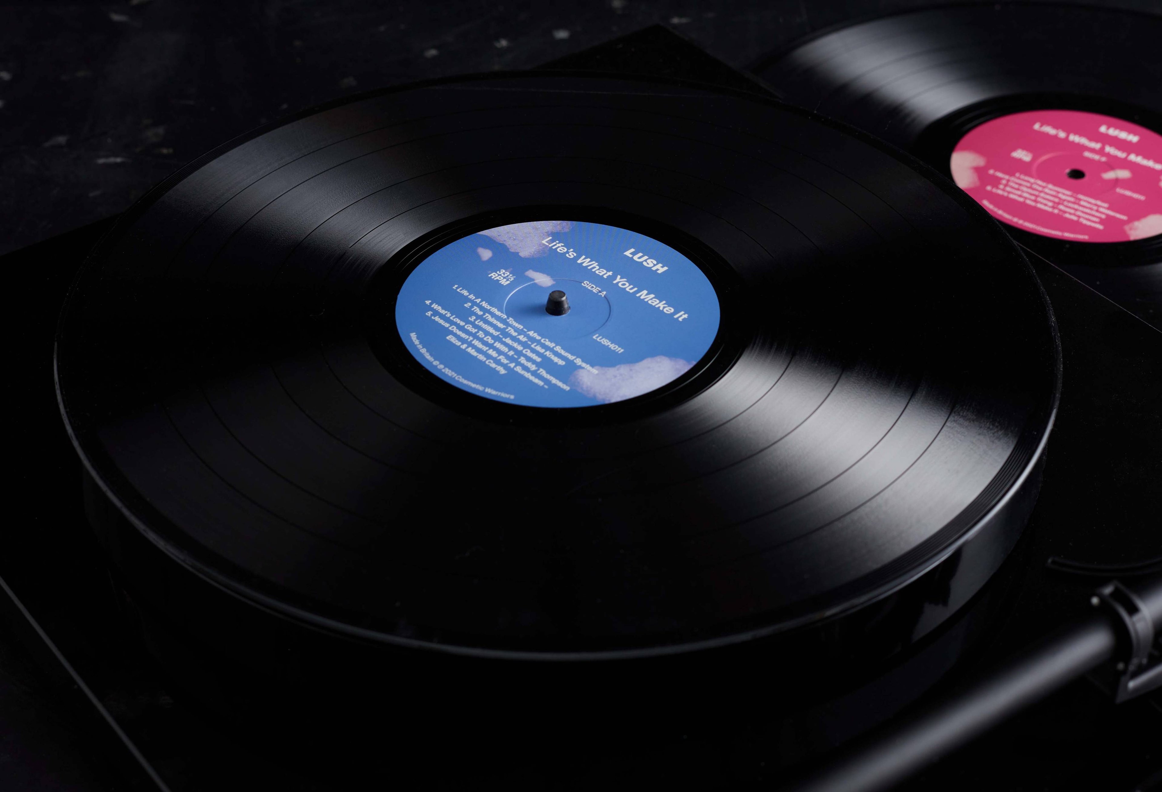 A close up of both records, one with a blue label and one pink, with the blue on a record deck.