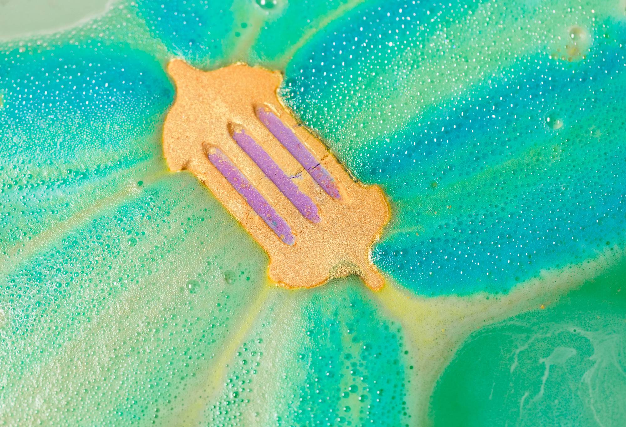 The bath bomb floats face up in green water, fizzing away and giving off light green and blue streaks.