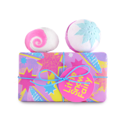Little Snow Fairy. A rectangular gift box wrapped in pink and purple paper with stars and streaks across, tied with thin, blue ribbon, and attached gift tag. Two Snow Fairy bath products sit on top of the gift box. 