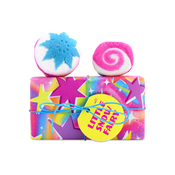 A Lush Little Snow Fairy gift set wrapped in colourful starry paper with a yellow tag, topped with a blue snowflake bath bomb and a pink swirled bubble bar