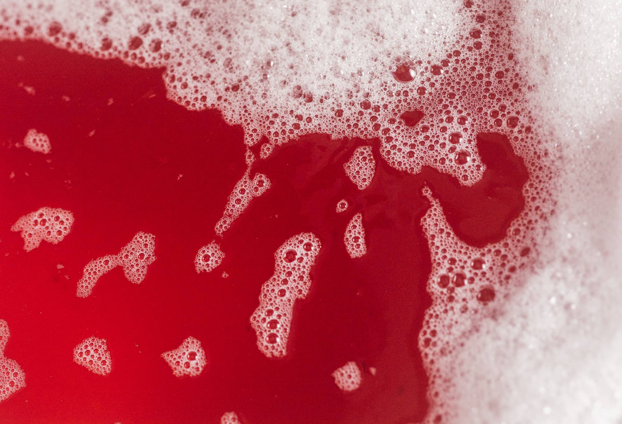 Image shows deep, blood-red coloured bathwater framed by thick bubbles.