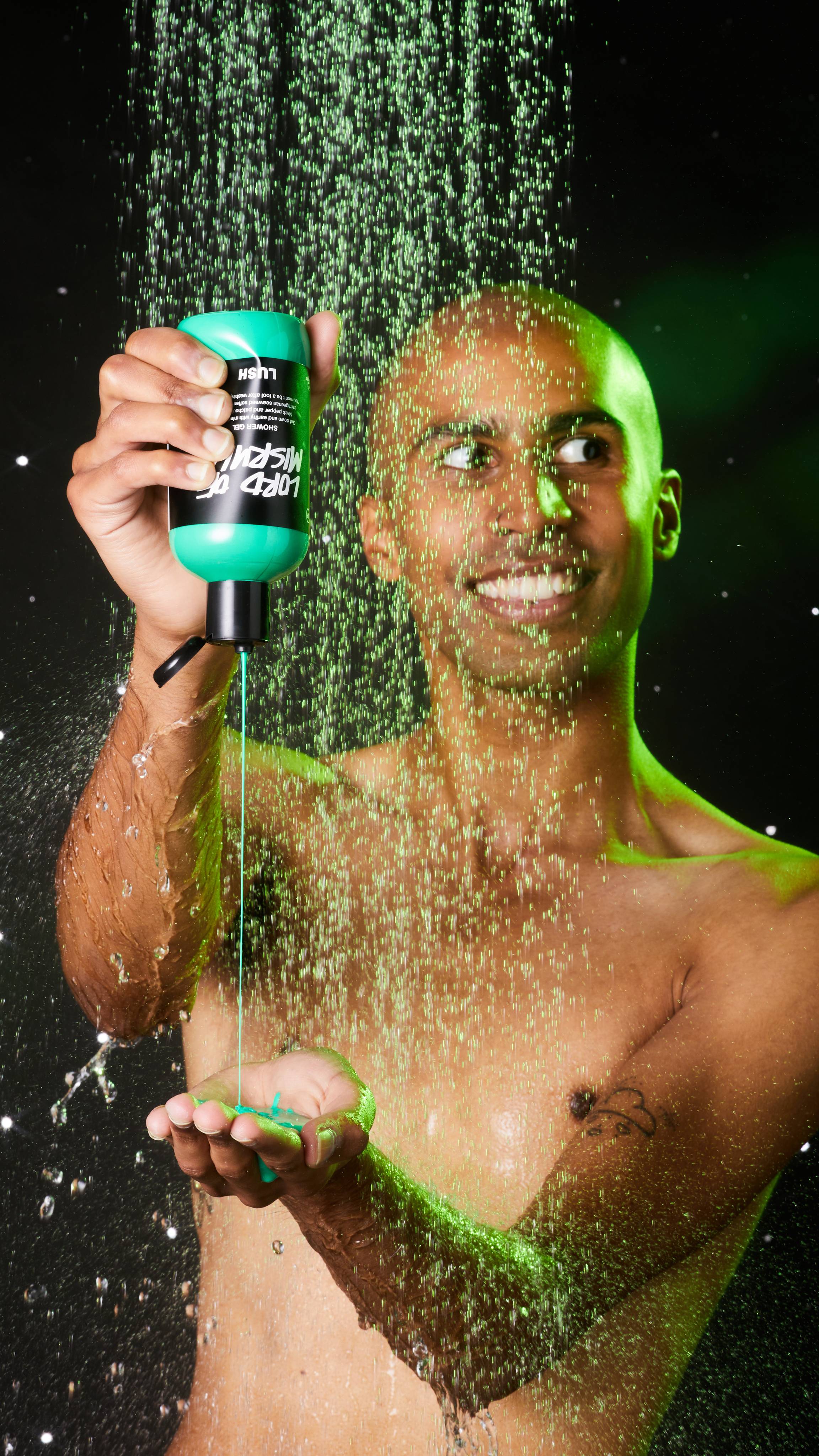 Image shows model in the shower squeezing the shower gel from the bottle into their hand on an emerald-green background.