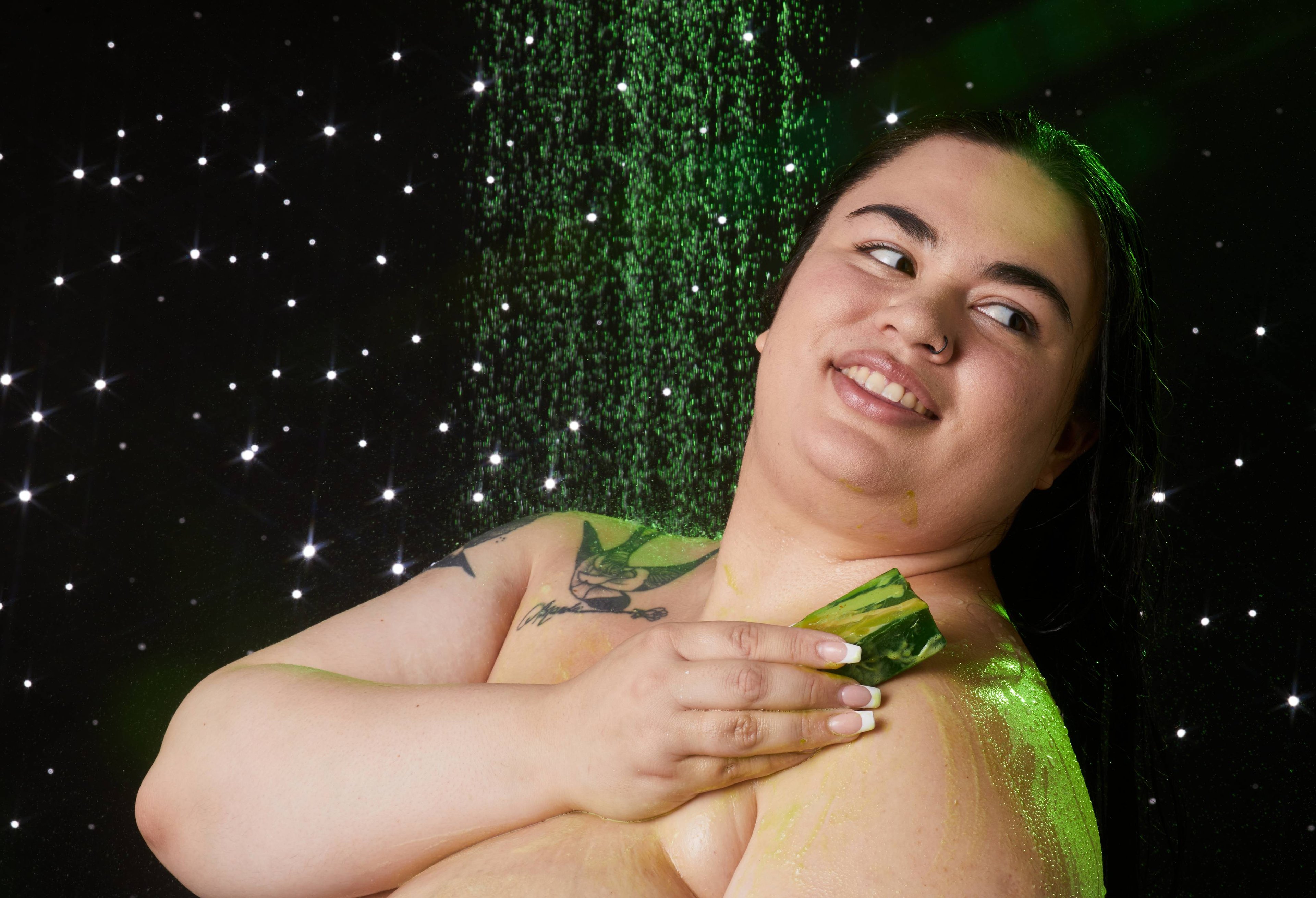 Model is stood under running shower water soothing the Lord of Misrule soap over their shoulder on a twinkling background.