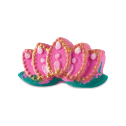 Lotus Blossom. A Diwali-themed, Lush bath bomb shaped like a fully bloomed, lotus flower. There are five, fanned pink petals shaped with gold detailing sitting on top of green leaves. 