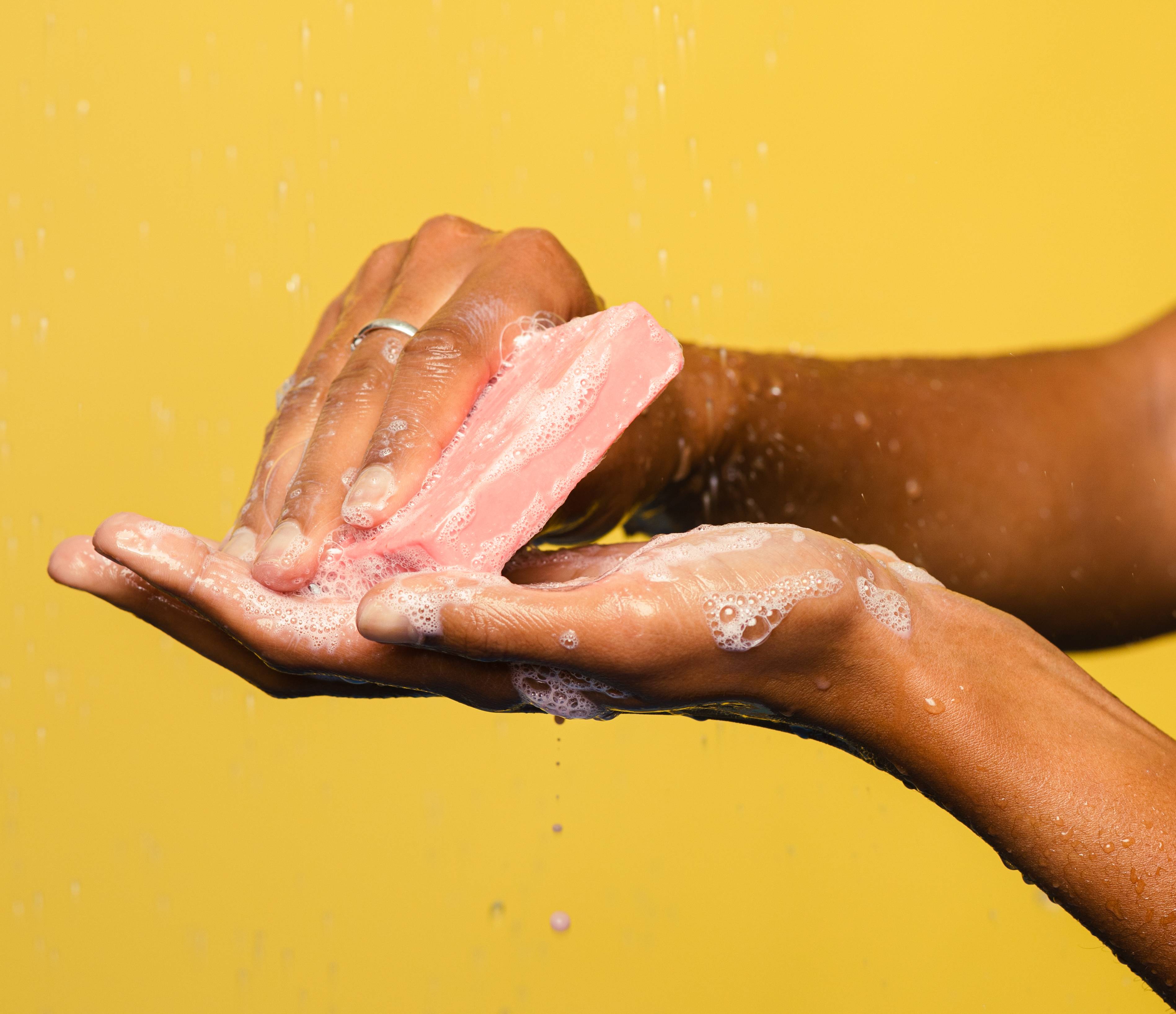 A bubbly close-up of Lotus Flower lathering up in a person's hands: it's a rosy pink soap.