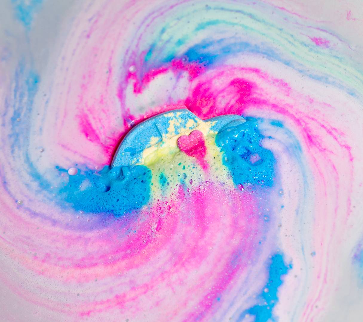 Love Bug bath bomb dissolves in the water leaving a swirling galaxy of vivid pinks, blues and yellows.