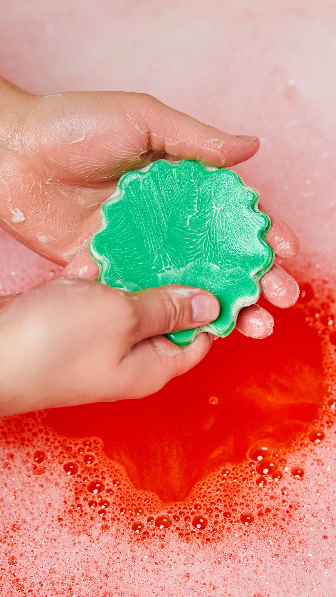 Image shows a close-up of the model using the green lettuce soap product portion as they create a lather in their hands. 
