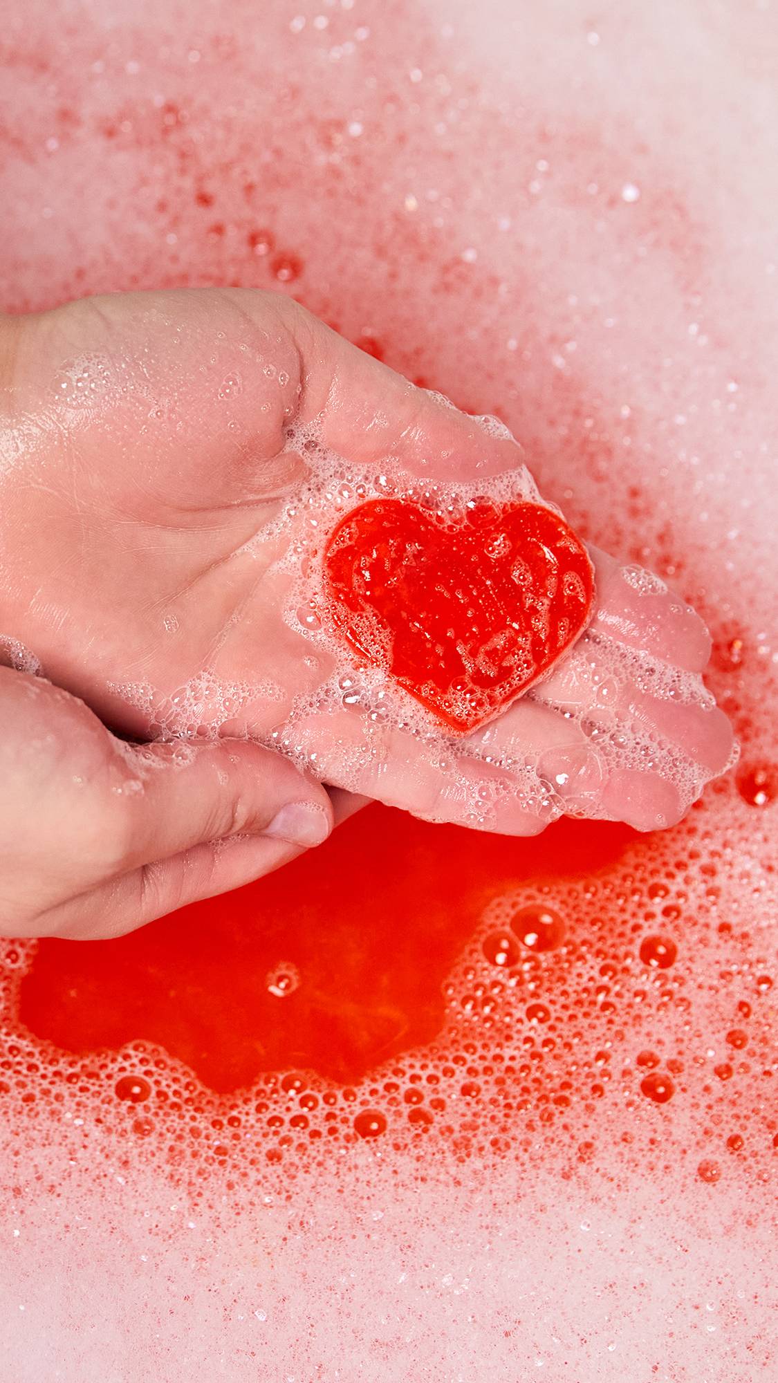 Image shows a close-up of the model using the love heart-shaped, tomato soap product portion as they create a soapy lather in their hands. 