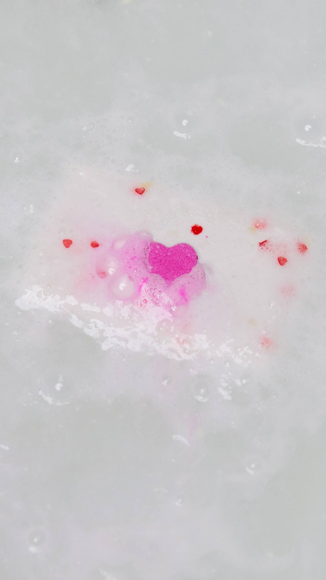 The Love Letter bath bomb has almost fully dissolved leaving behind dots of tiny, red, heart confetti and a single large pink heart.