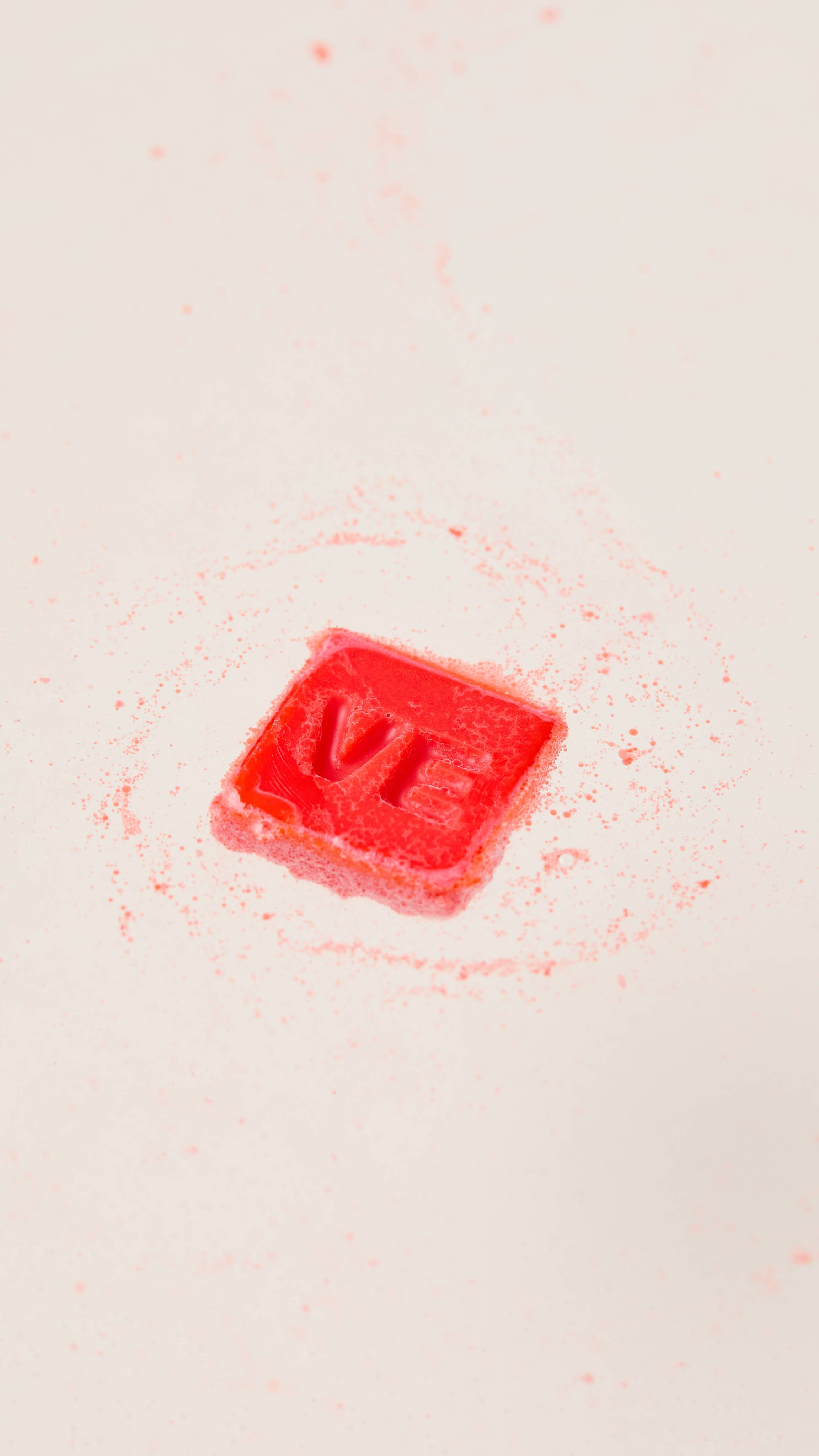 The image shows a single square of the deep red Love Spell Lush Melt as it begins to melt in the bath water. 